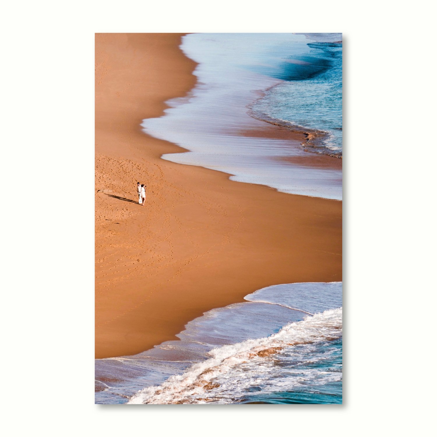 A couple are surrounded by sweeping golden sands and gentle blue-green waves on the shore. Vertical variant.
