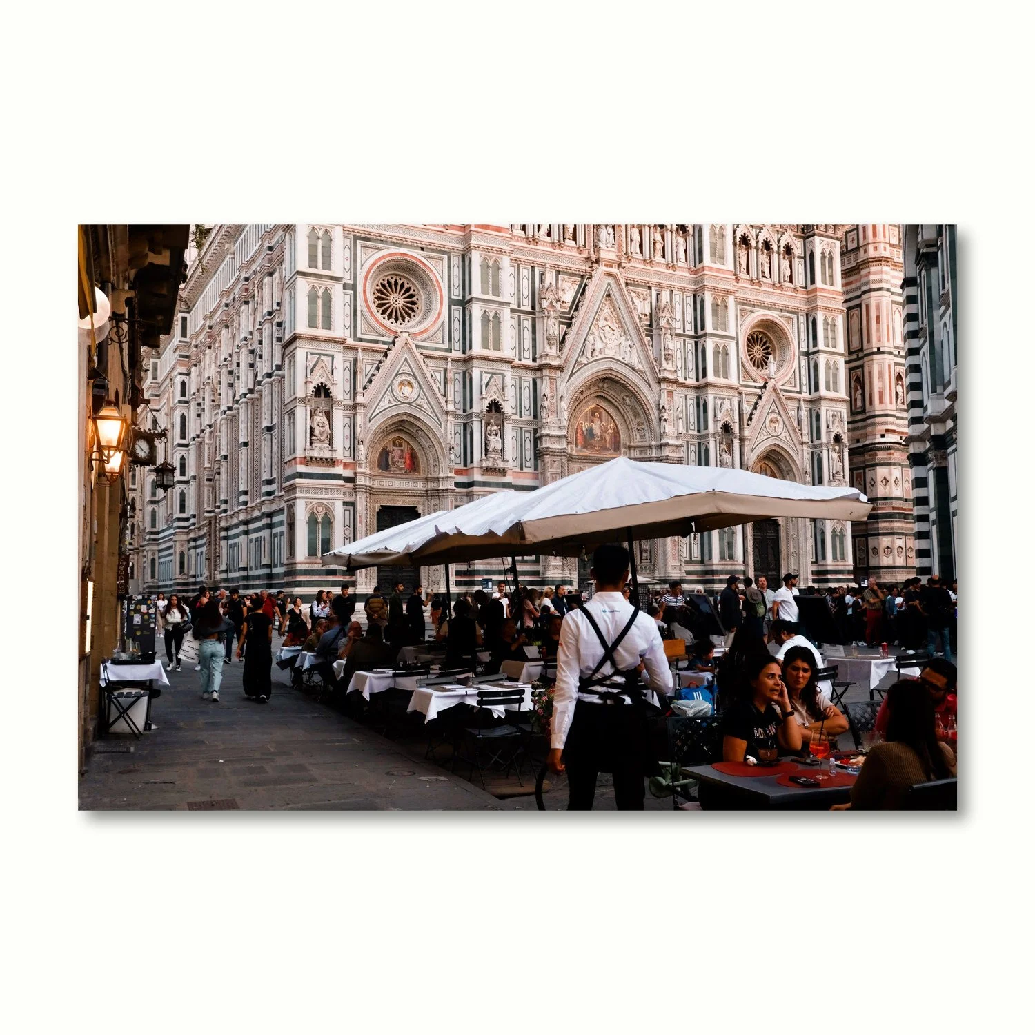 A waiter in the foreground surveys his customers sitting at tables in the magnificent Il Duomo piazza.