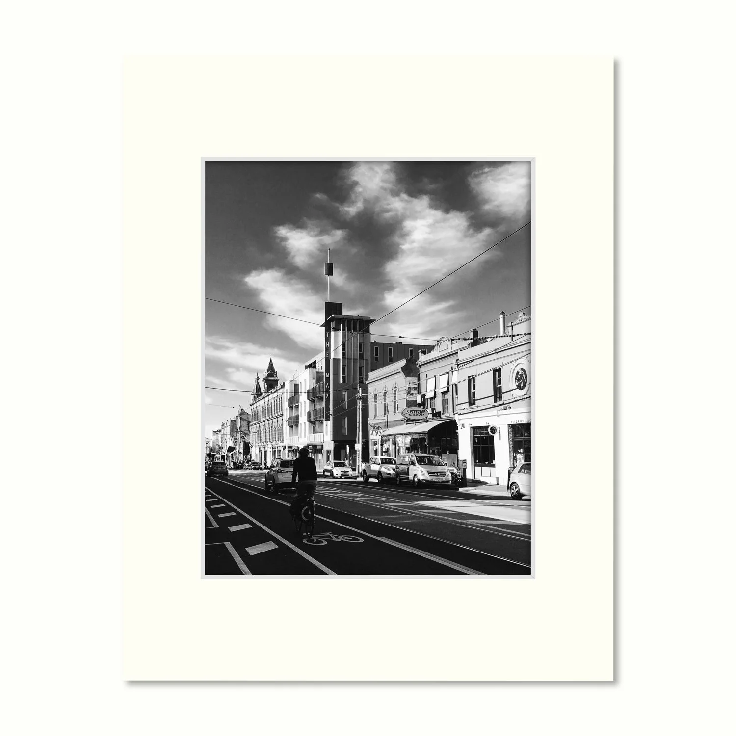 A B&W print of streetscape - Brunswick Street, Fitzroy, featuring a cyclist and surrounding buildings presented in an attractive mount.