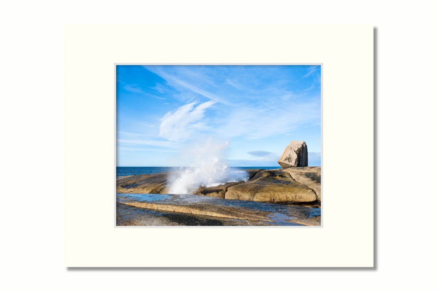 A photo of a rocky coastal scene where a blowhole shoots water into the air, appearing to match up with the cloud formations.
