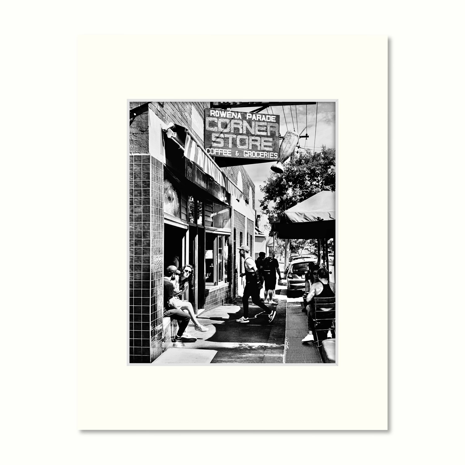B&W photo of a popular corner store, turned cafe in Richmond, featuring sidewalk seating and historic signage, presented mounted.