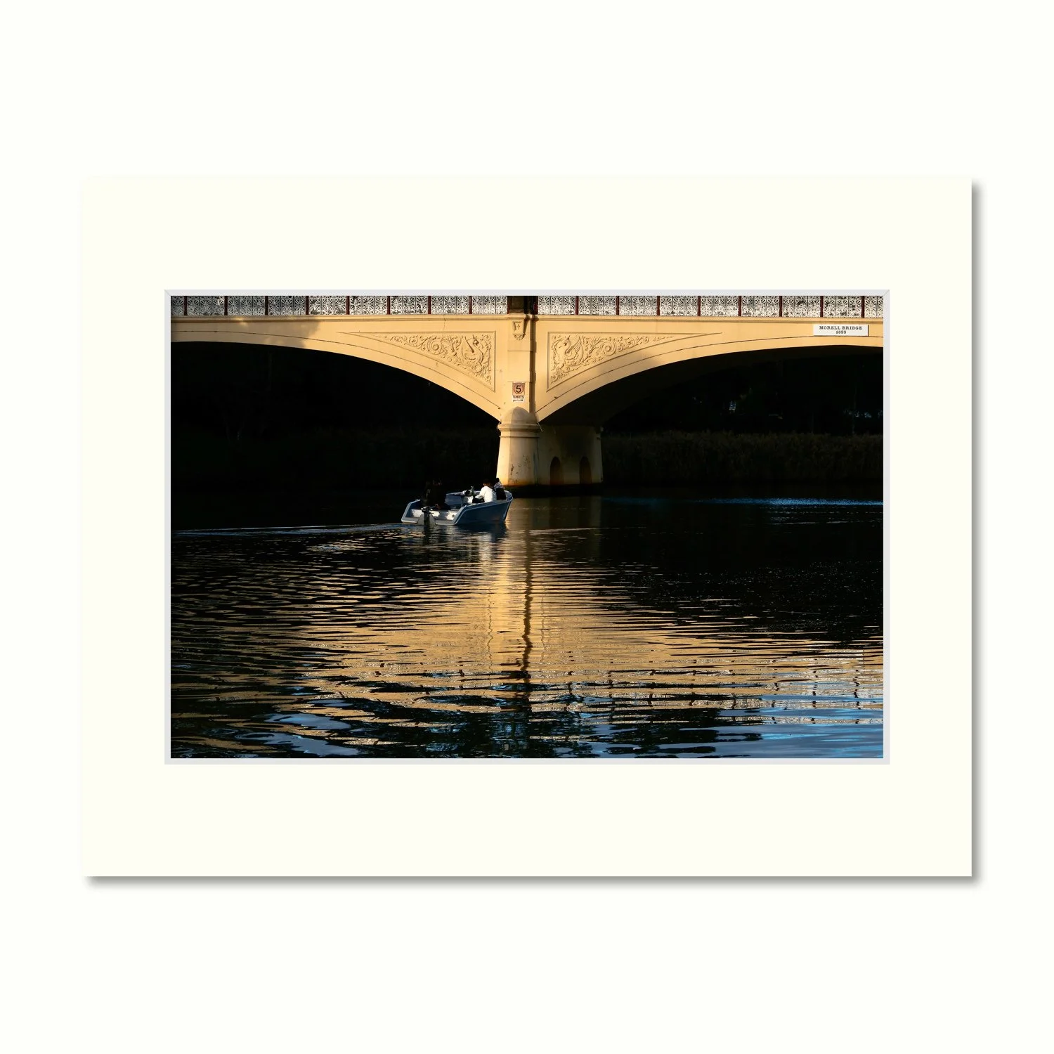 A frame mount containing a print of the Morell Bridge arches in Melbourne featuring golden ripples on the Yarra as a boat passes.
