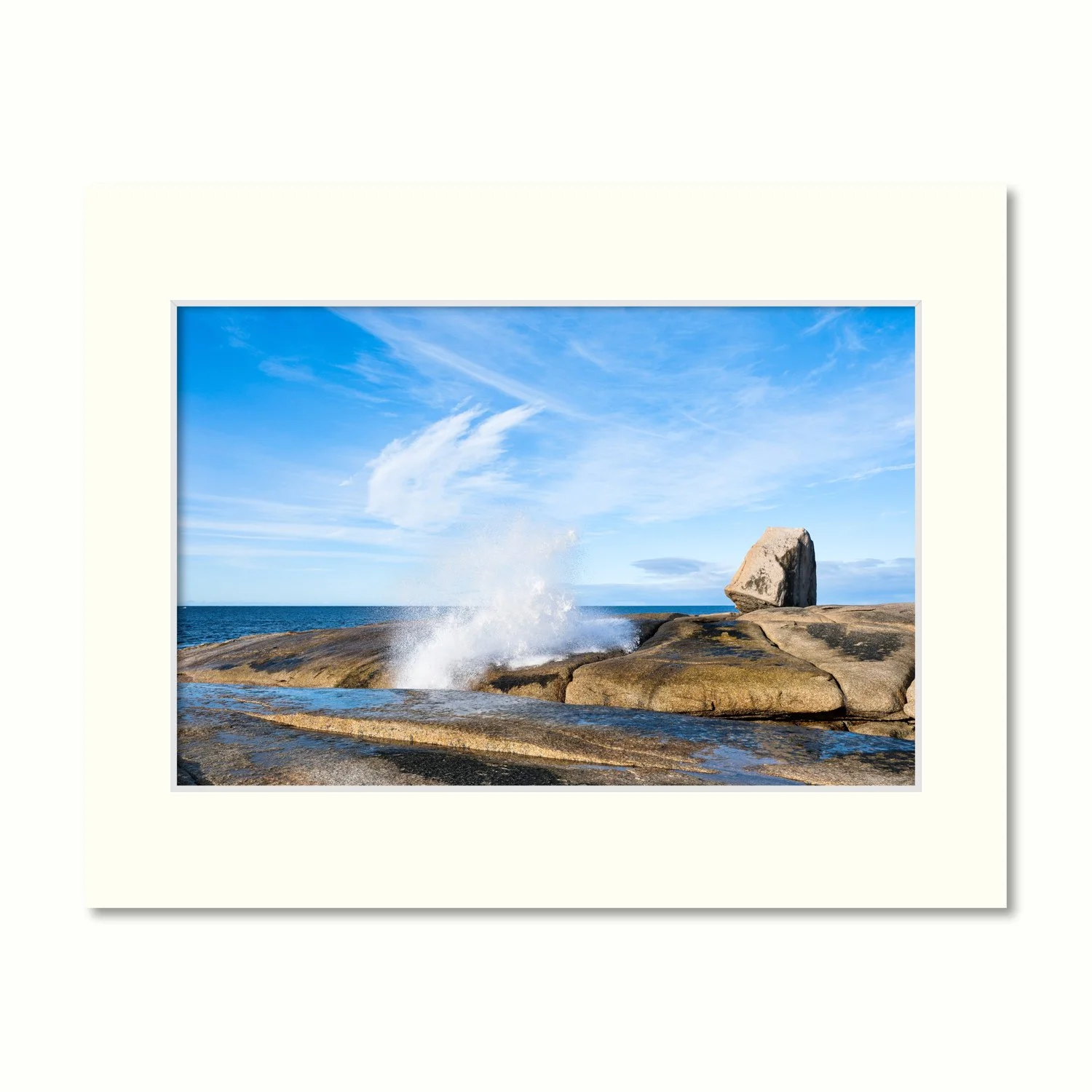 A frame mount containing a photo of a blowhole shooting water upwards to meet the cirrus clouds in a beautiful blue sky.