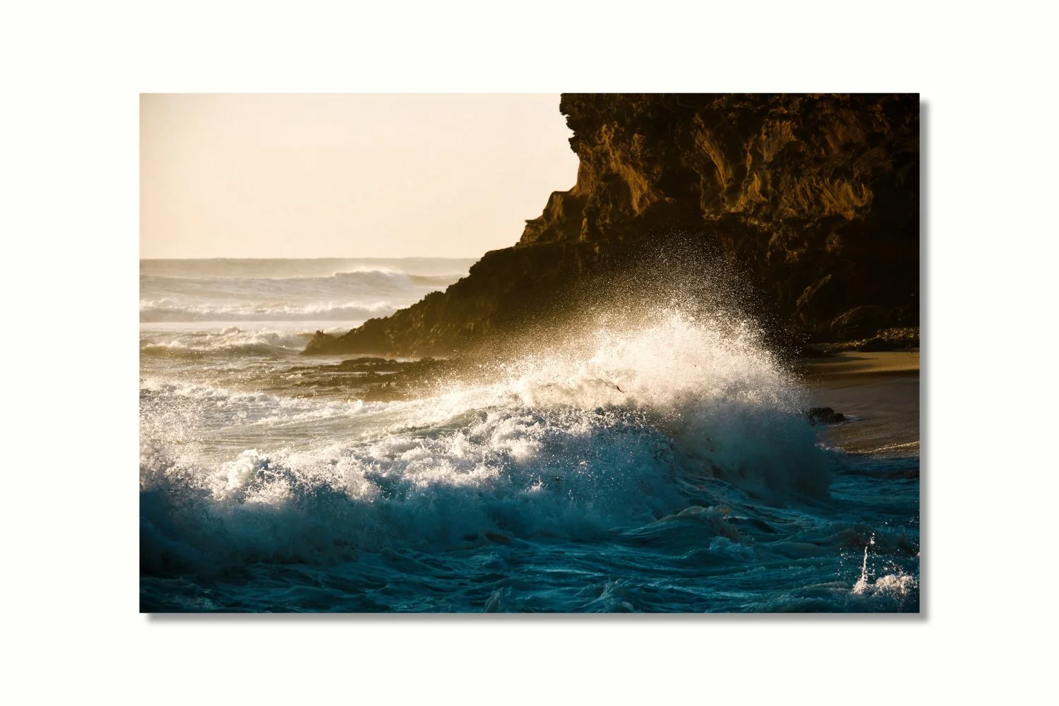 A photo of a wave crashing near the shore against a rocky cliff background.