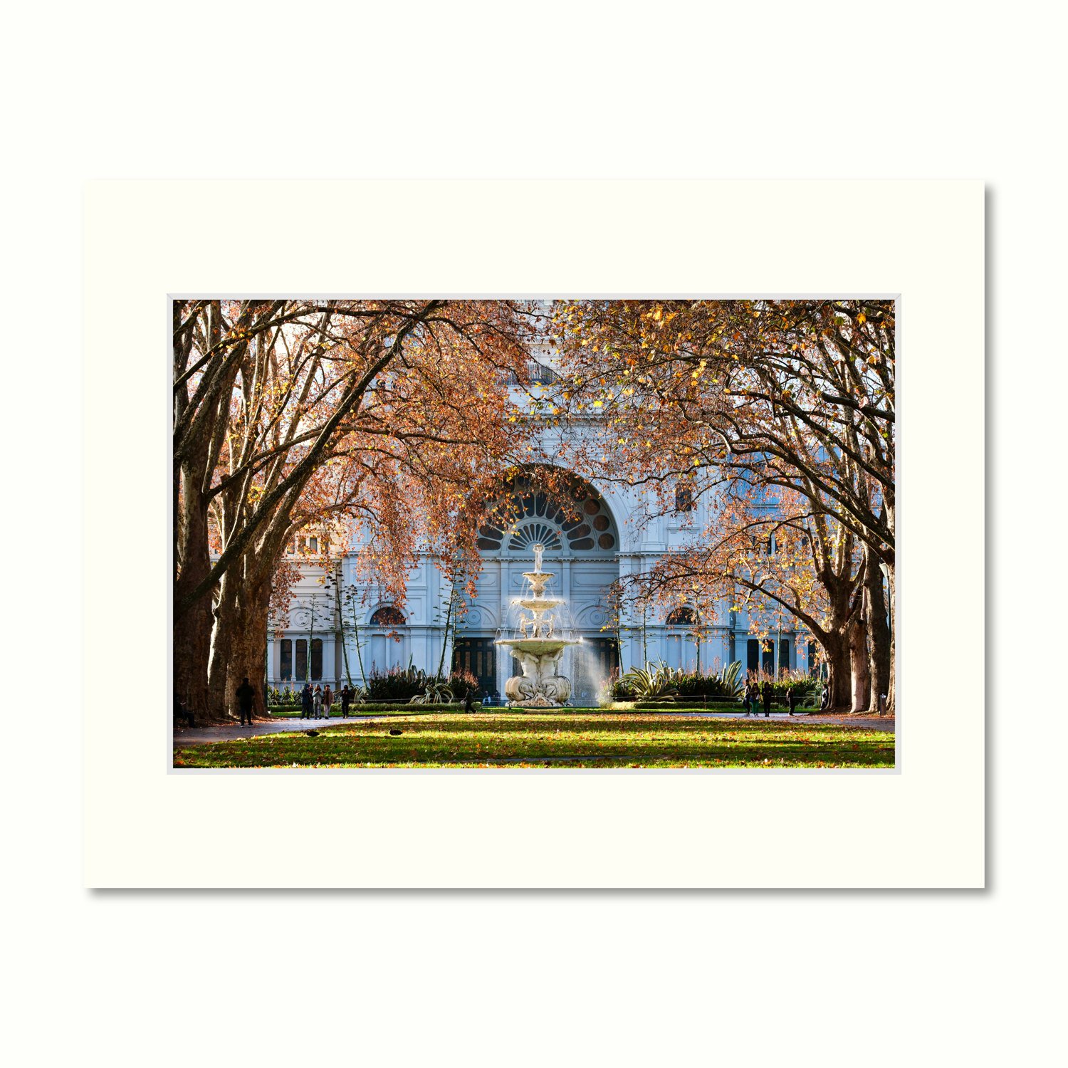A mount containing a print of the Royal Exhibition Building framed by golden autumn trees and a flowing fountain in Carlton Gardens.