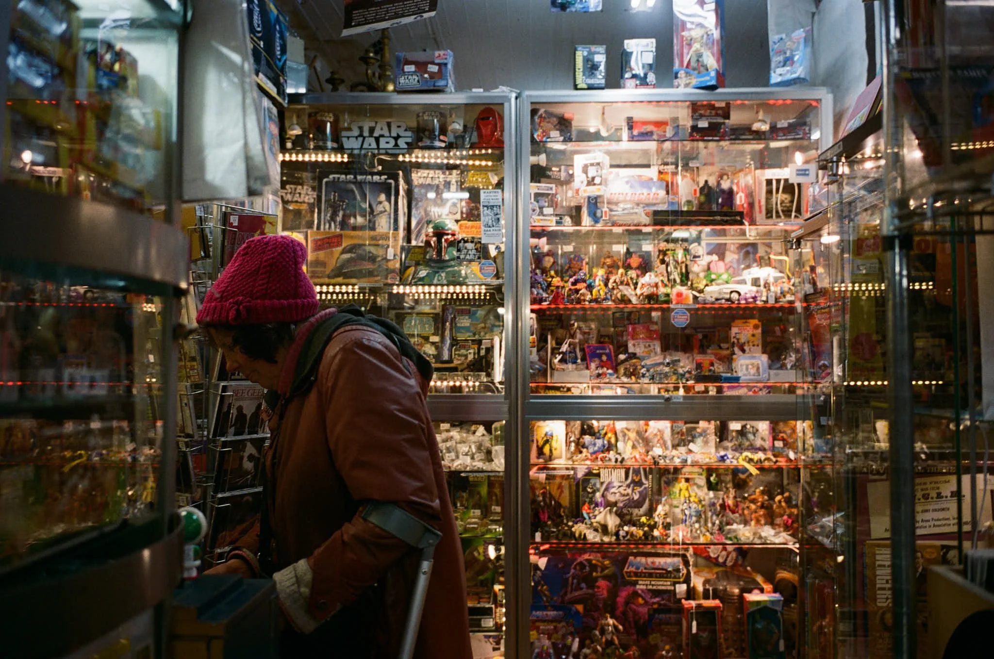 A person shopping at a vintage toy store with glass display cases filled with action figures, collectibles, and Star Wars memorabilia.