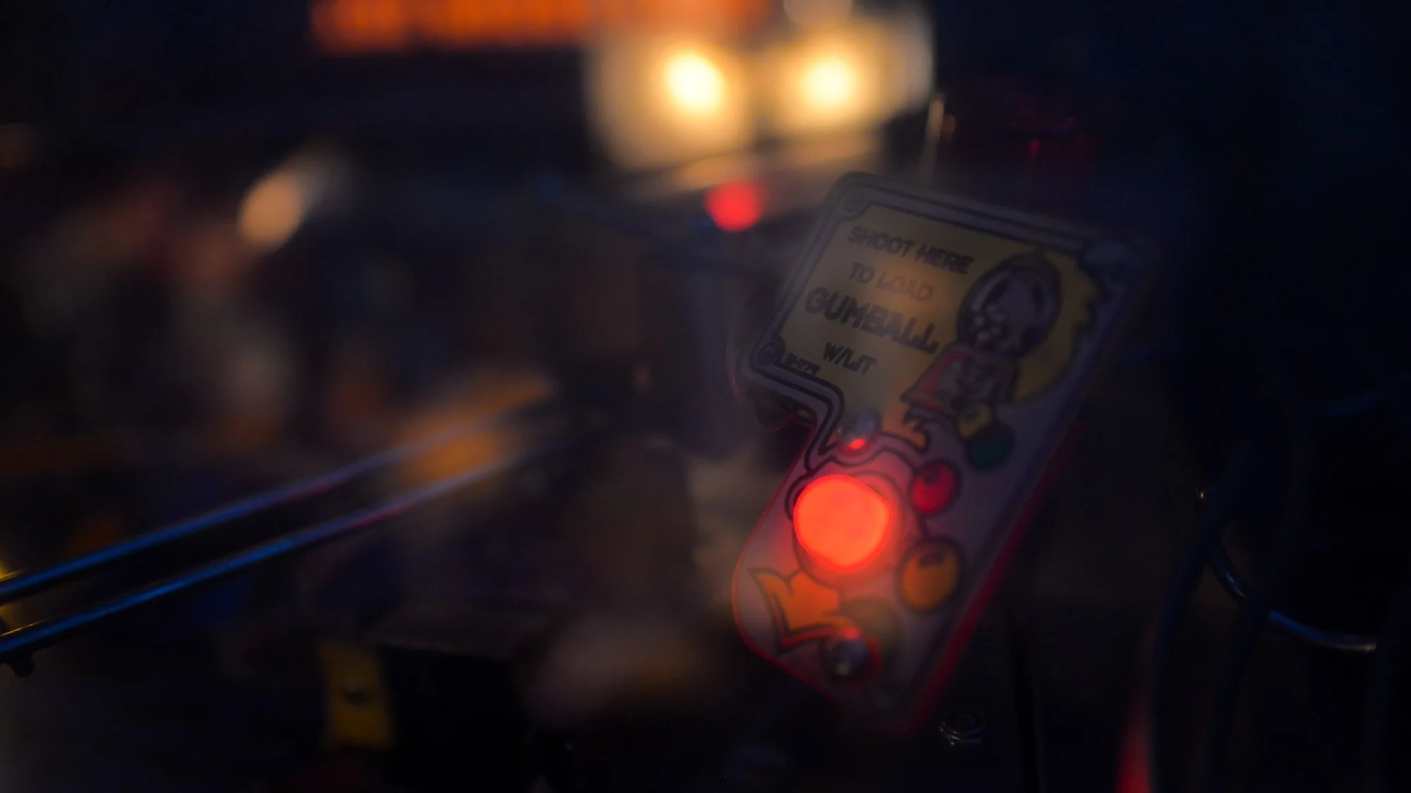 A close-up view of a vintage pinball machine with illuminated lights and a playfield, showing a part of one of the game cards with a cartoon character and instructions.