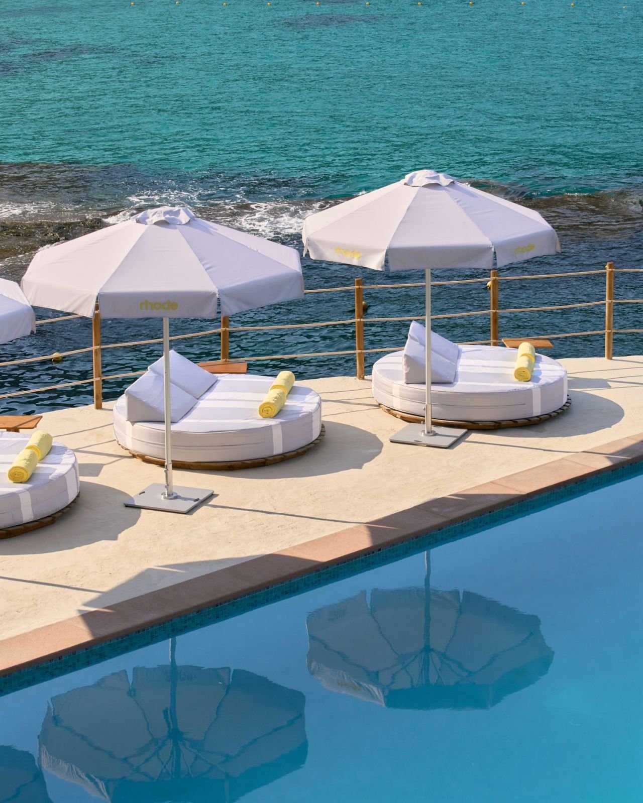 Poolside lounge chairs with yellow towels, white umbrellas, and a view of the ocean in the background.
