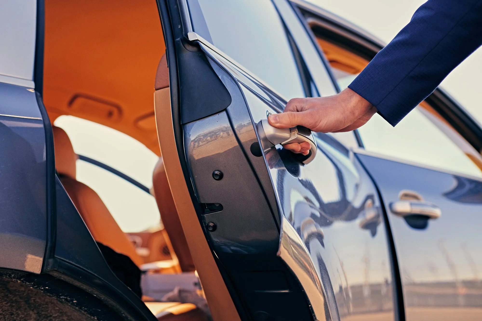 Person opening the rear door of a dark-colored car with leather interior, during daylight.