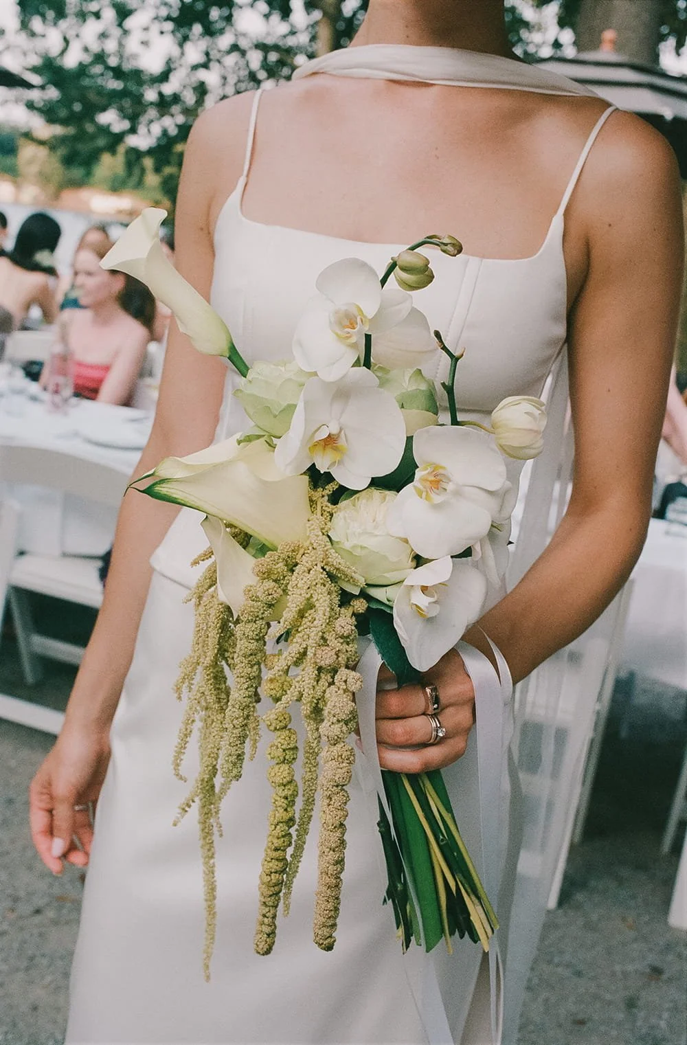 A bride holding a bouquet of white orchids, calla lilies, and other cream-colored flowers at a wedding reception.