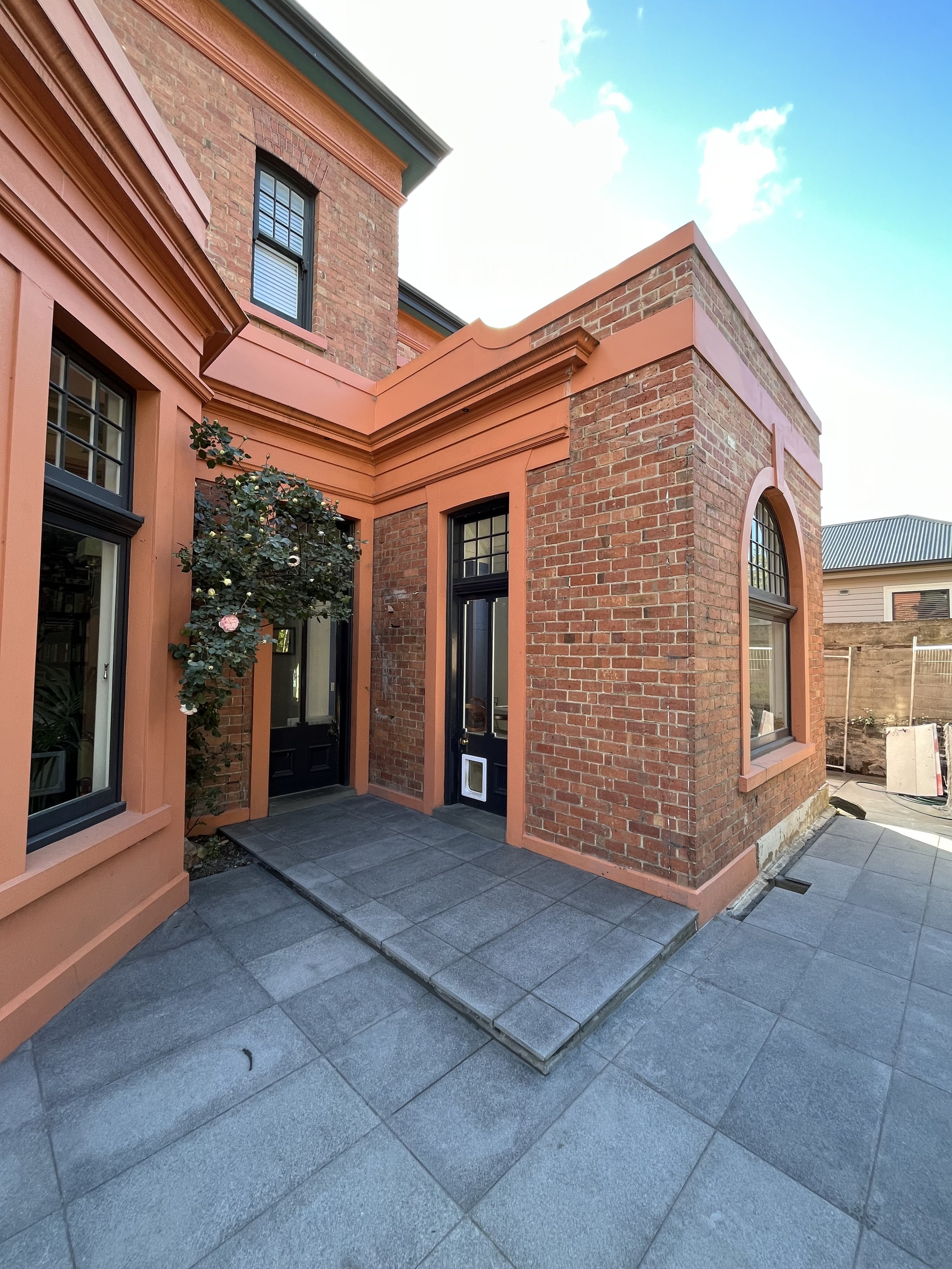 Exterior of a brick house with peach trim and large windows, featuring a small garden area and tiled pathway.