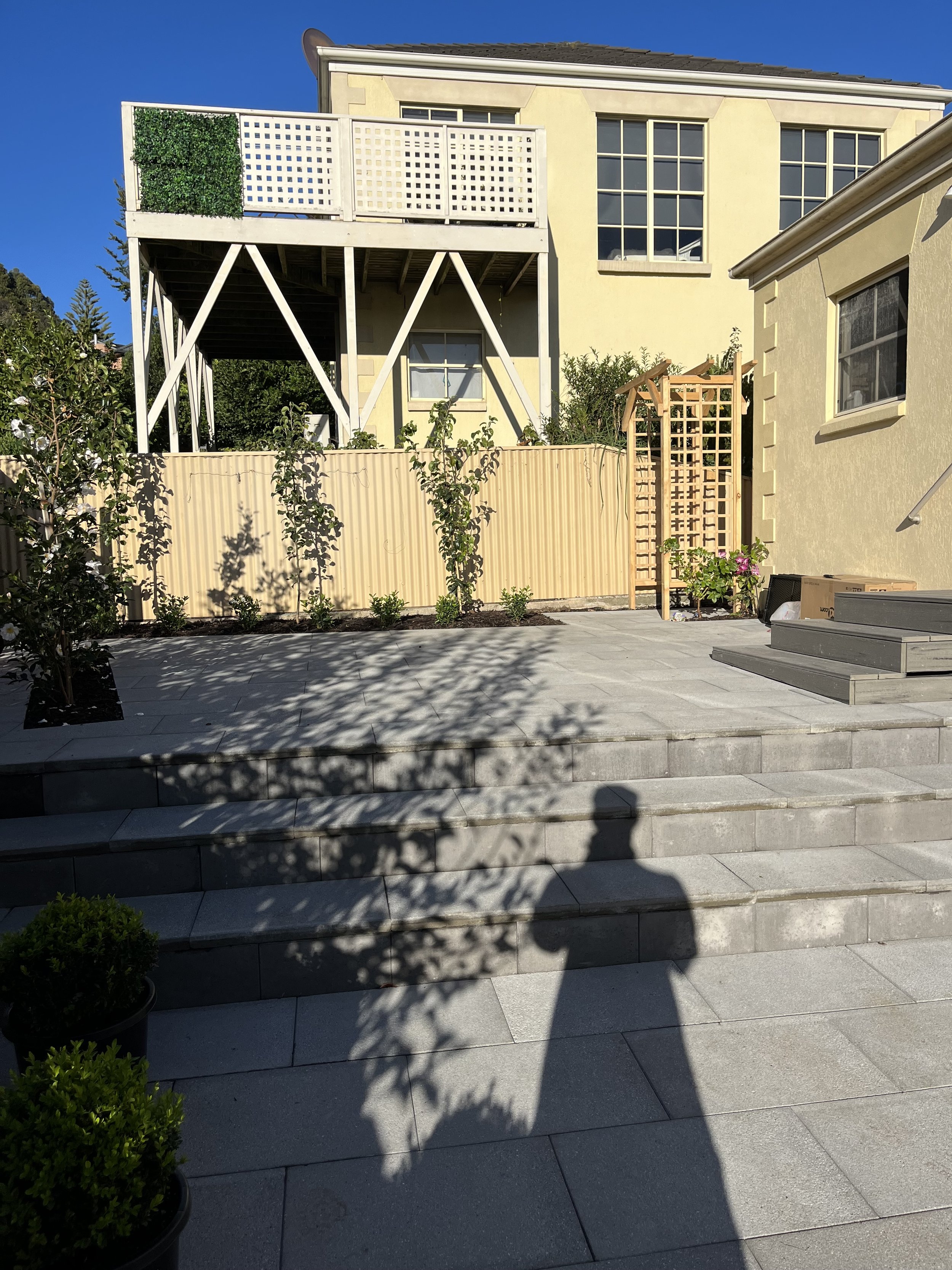 Residential backyard with stone patio, elevated balcony, and trellis with wooden pergola