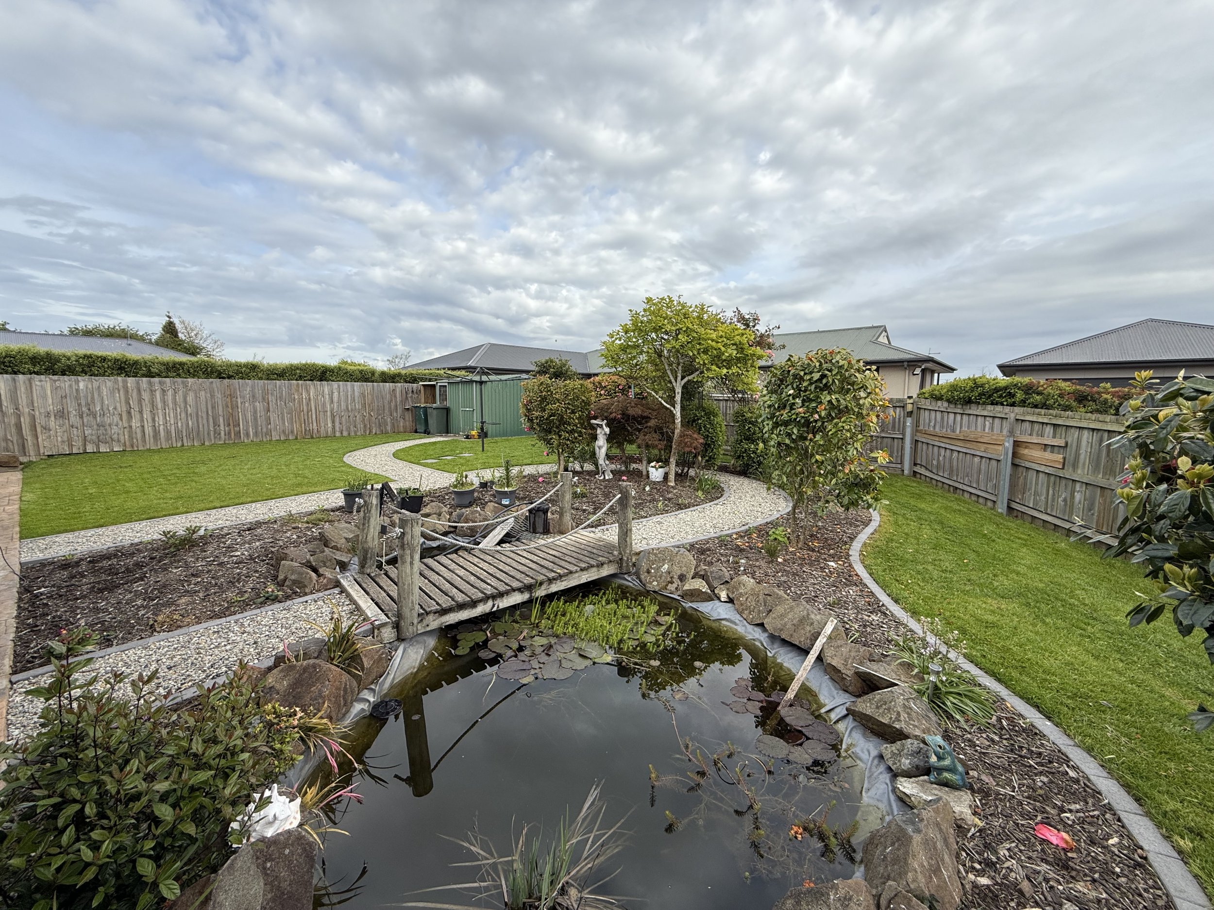 Backyard garden with a pond, wooden bridge, and landscaped pathways.