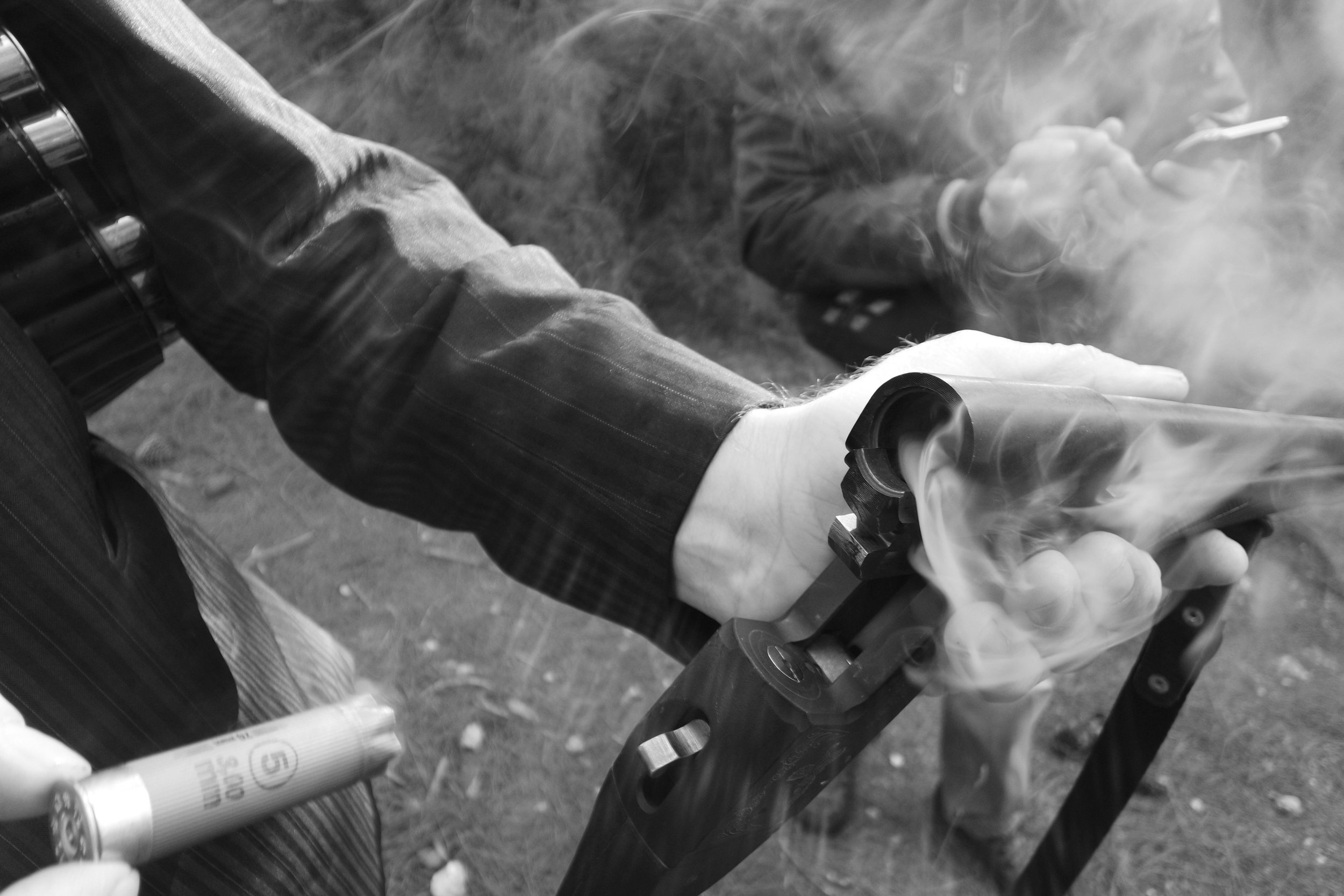 A person holding a smoking revolver gun with one hand and a spray can in the other, outdoors on a grassy area.
