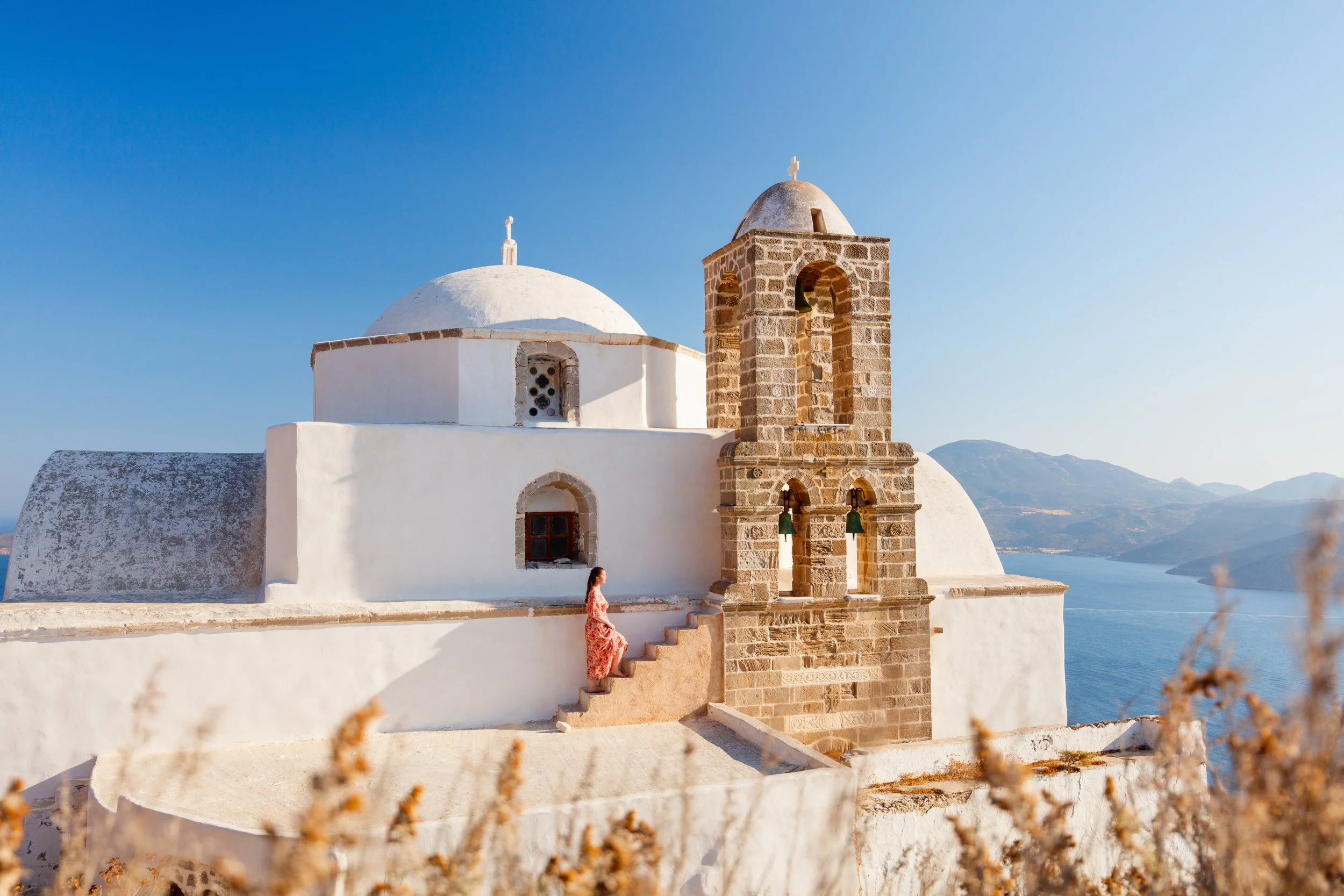 A white church with a rounded dome and a small bell tower, a panoramic view of Greece