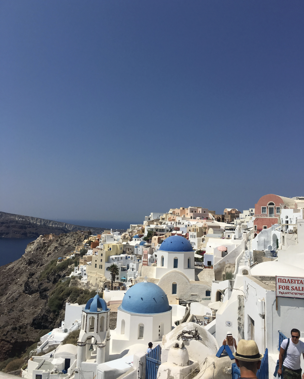 View of blue domed churches and houses built into cliffs in Santorini, Greece, captured during Angela's destination research trip