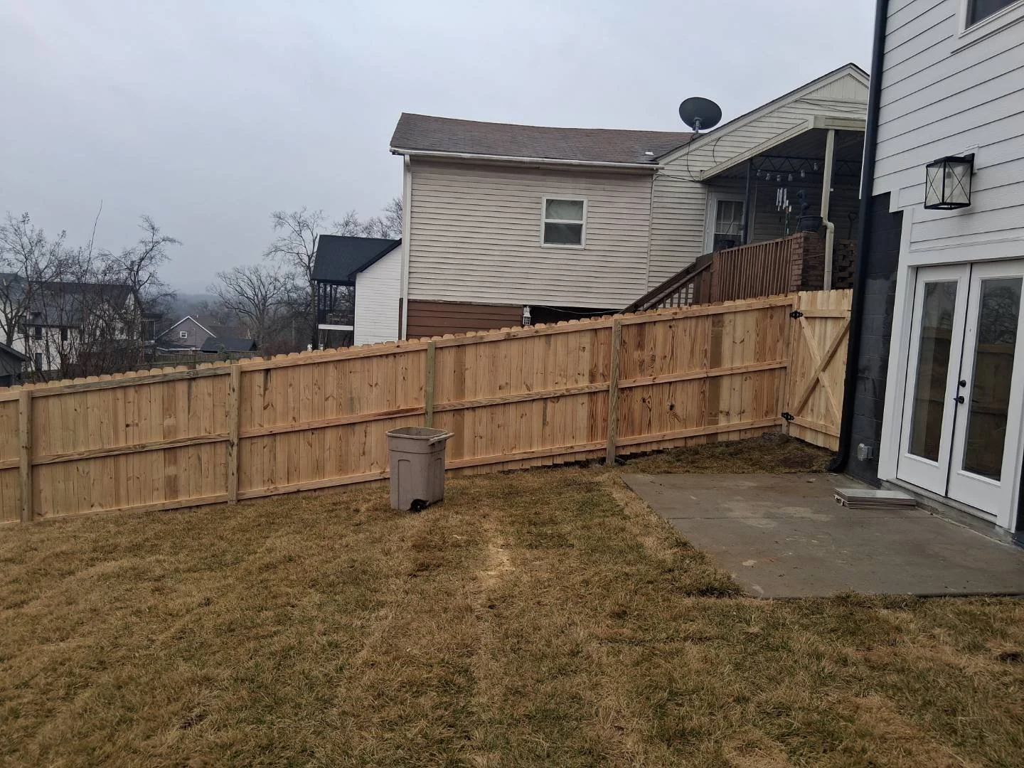 New wood privacy fence installed along a residential backyard with a gate next to the house