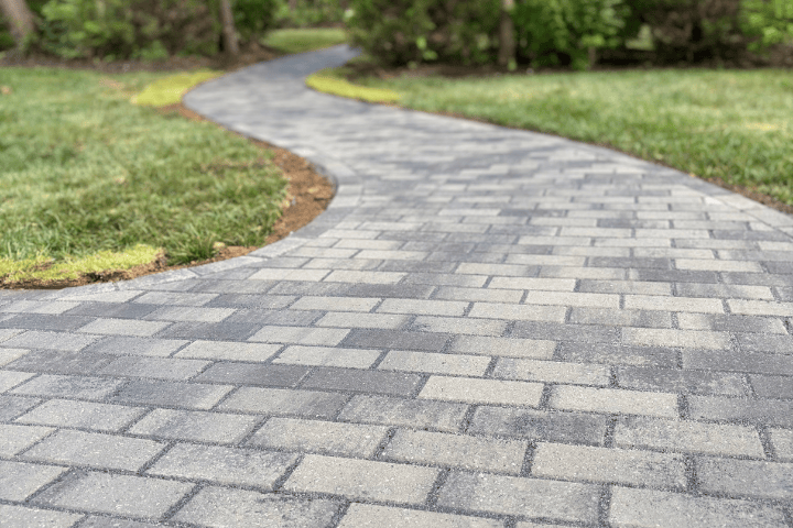 A winding outdoor brick walkway with grass on both sides and trees in the background.