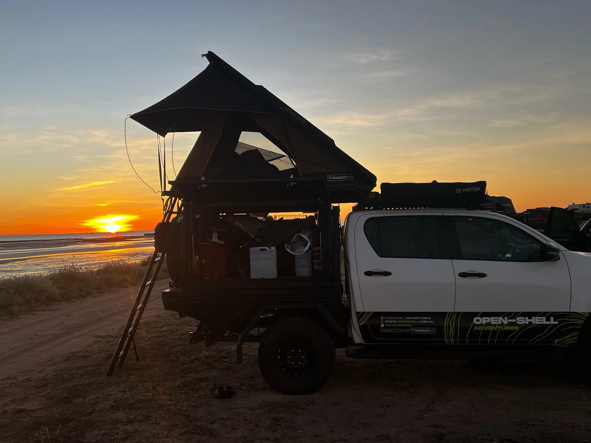 Open Shell Adventures 4x4 camper parked beside red dirt cliffs in Western Australia, showcasing premium rooftop tent and touring gear for rugged hire journeys