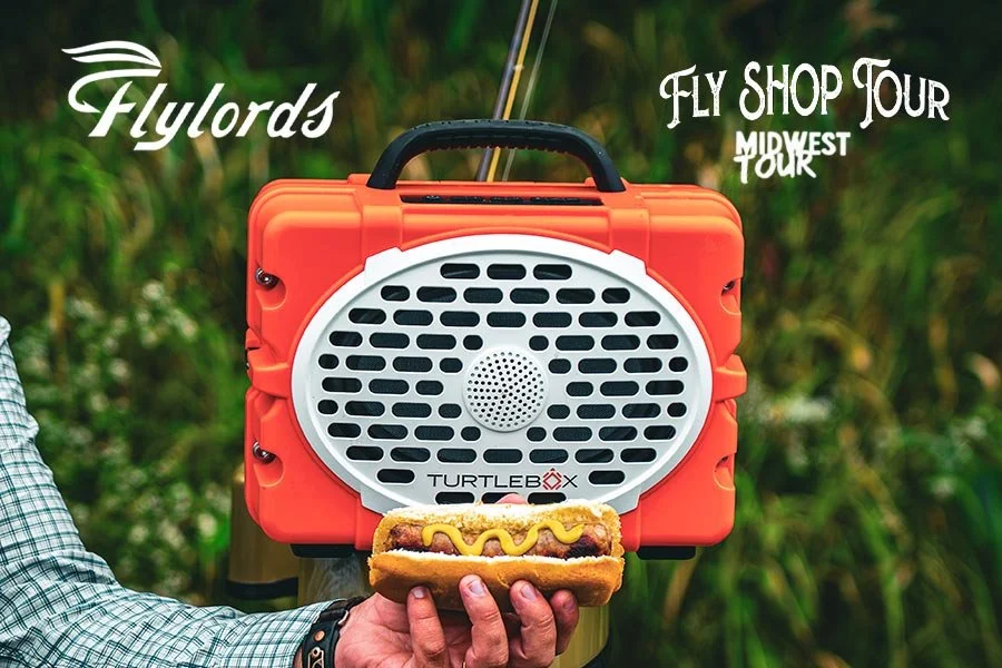 Male handing holding a brat in front of Turtlebox speaker with a FLylords logo in the upper left corner and the Fly Shop Tour Midwest Tour logo in the upper right