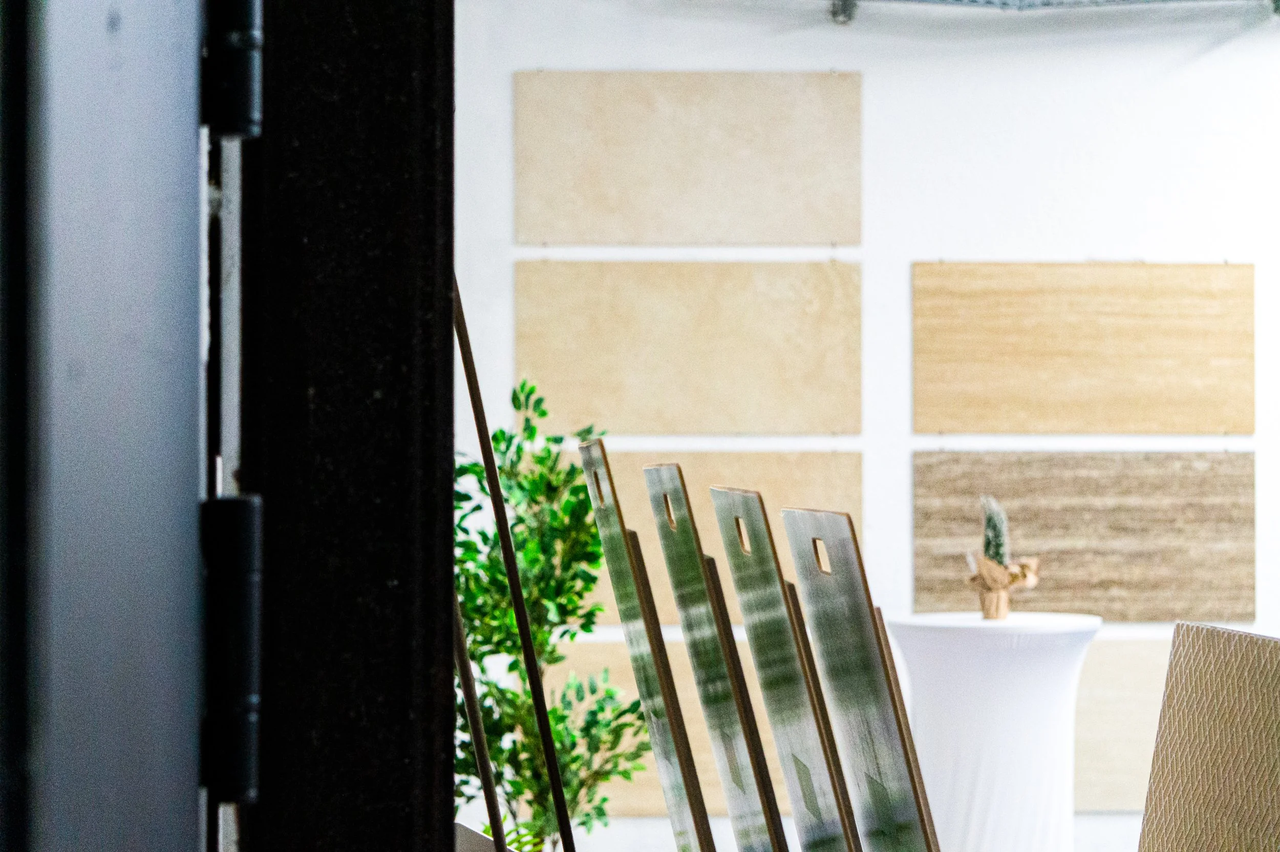 Innenansicht eines Raumes mit mehreren Holzproben an der Wand, einem großen weißen Blumentopf mit einer Pflanze und einem beige Sitzmöbel. Aufgenommen von Hilal Studios.