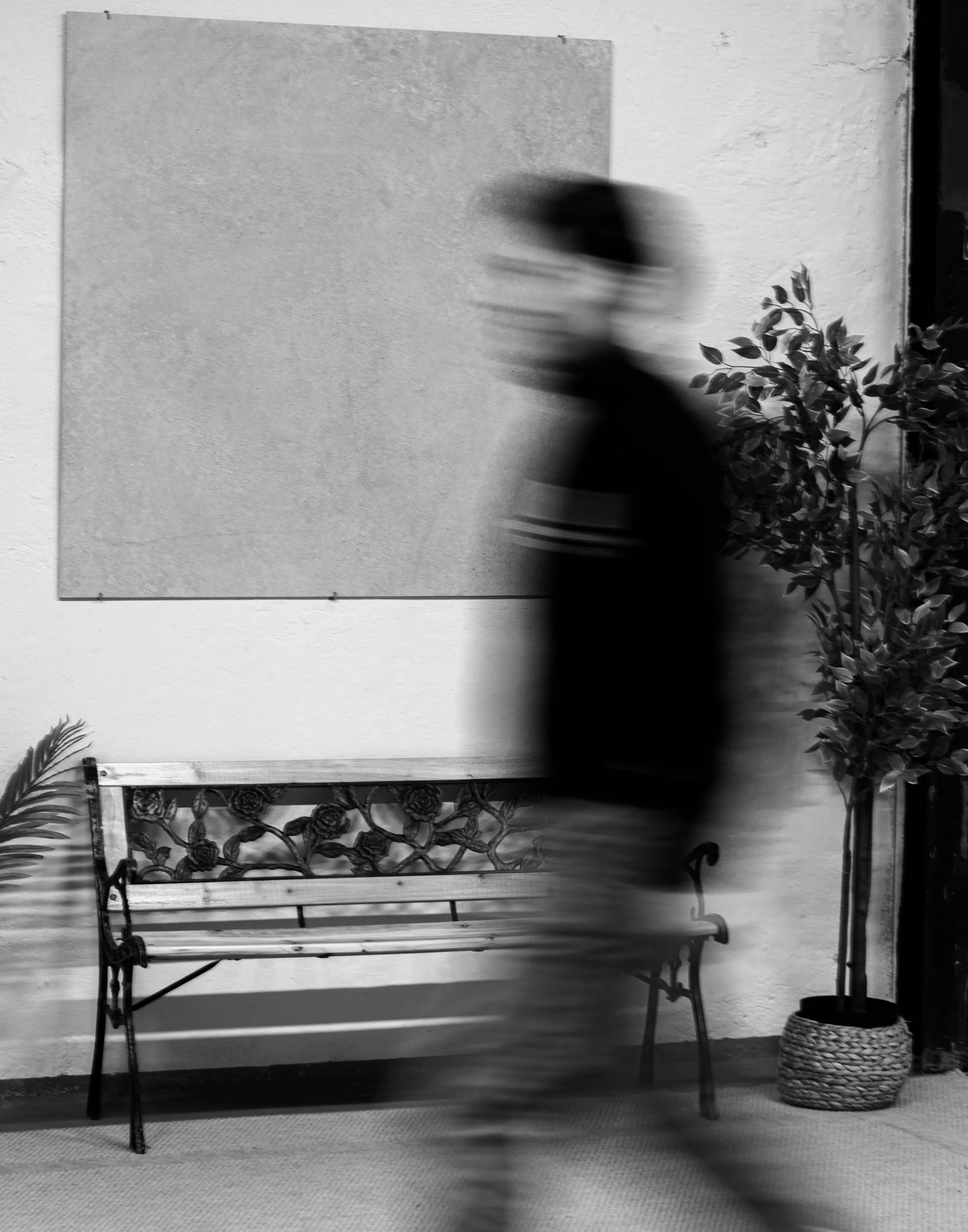 Eine verschwommene Person läuft an einer Bank und einer Pflanze in einem Innenraum vorbei, im Hintergrund eine weiße Wand mit einer großen Fliese. Aufgenommen von Hilal Studios.