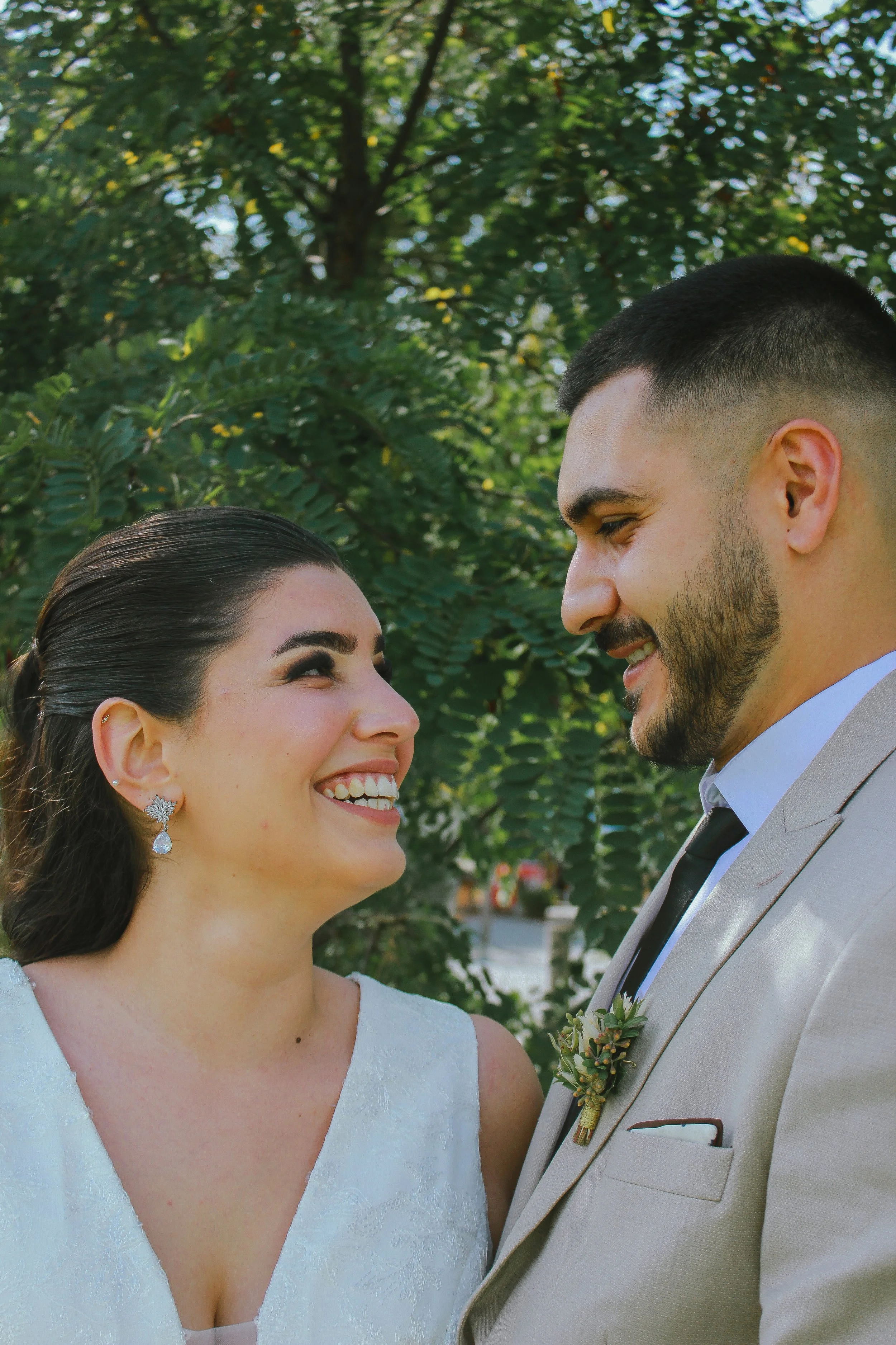 Ein Brautpaar lächelt sich bei einer Hochzeit im Freien an, umgeben von Bäumen. Aufgenommen von Hilal Studios.