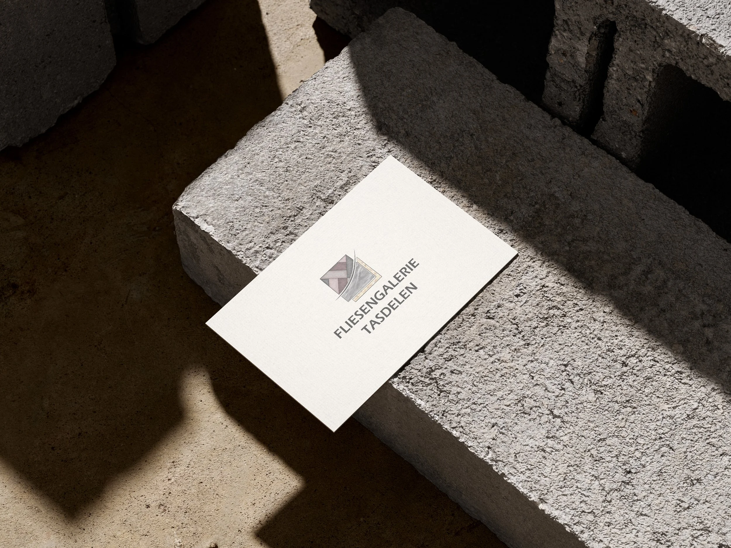 Weißer Firmenprospekt mit Logo und Schrift 'Fliesengalerie Taschen' liegt auf grauem Betonblock. Erstellt von Hilal Studios.
