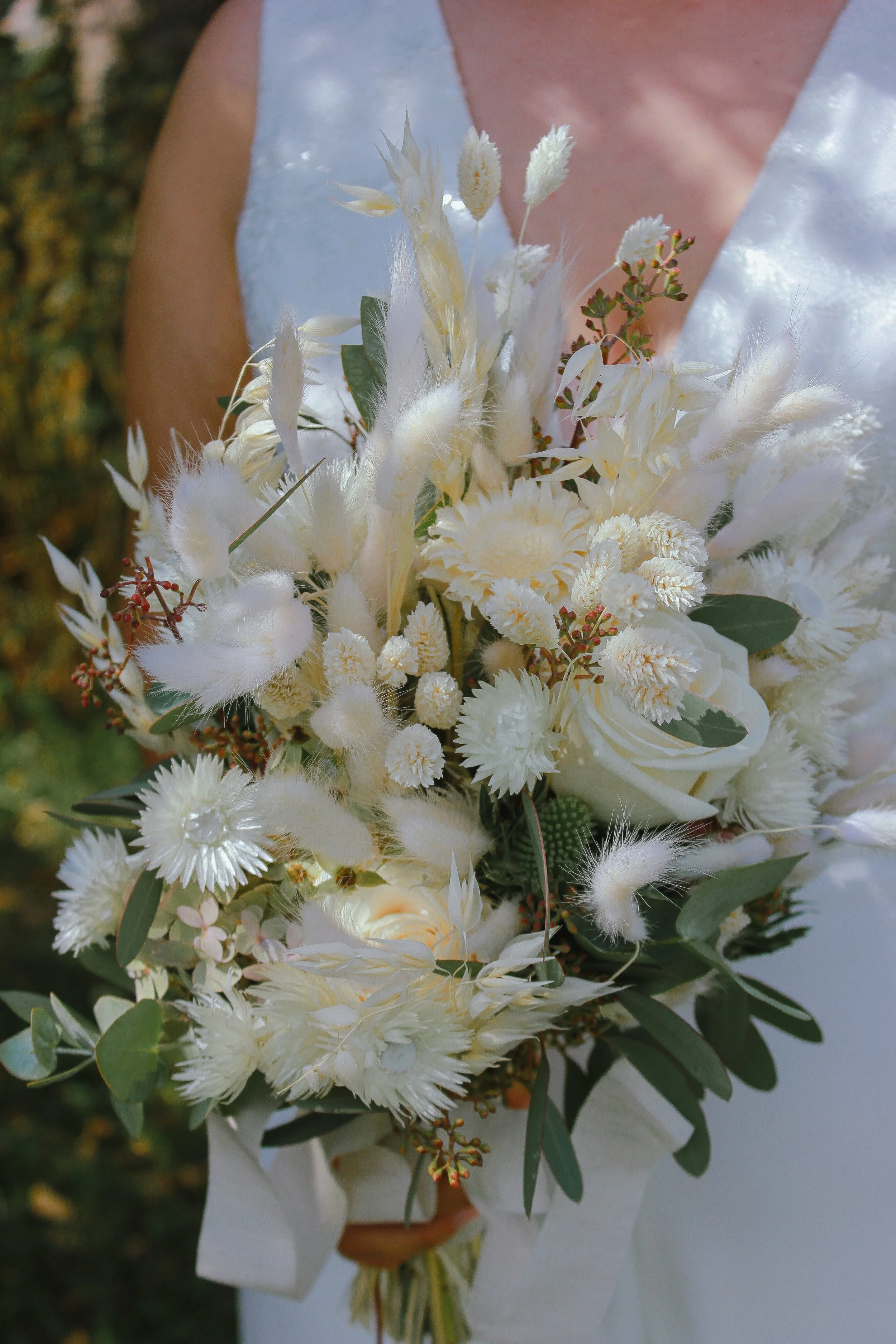 Eine Braut hält einen weißen Hochzeitsstrauß mit verschiedenen weißen Blumen und grünen Blättern. Aufgenommen von Hilal Studios.