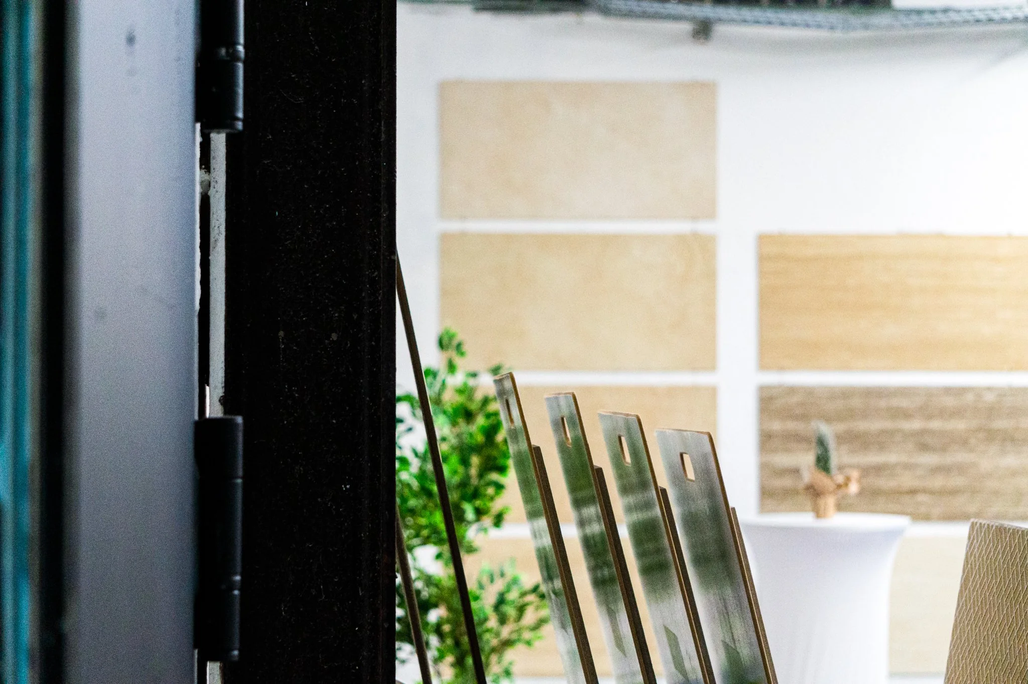 Innenansicht eines Raumes mit mehreren Holz- oder Metallstühlen, einer Pflanze und einer Wand mit gestreiften Paneelen. Aufgenommen von Hilal Studios.