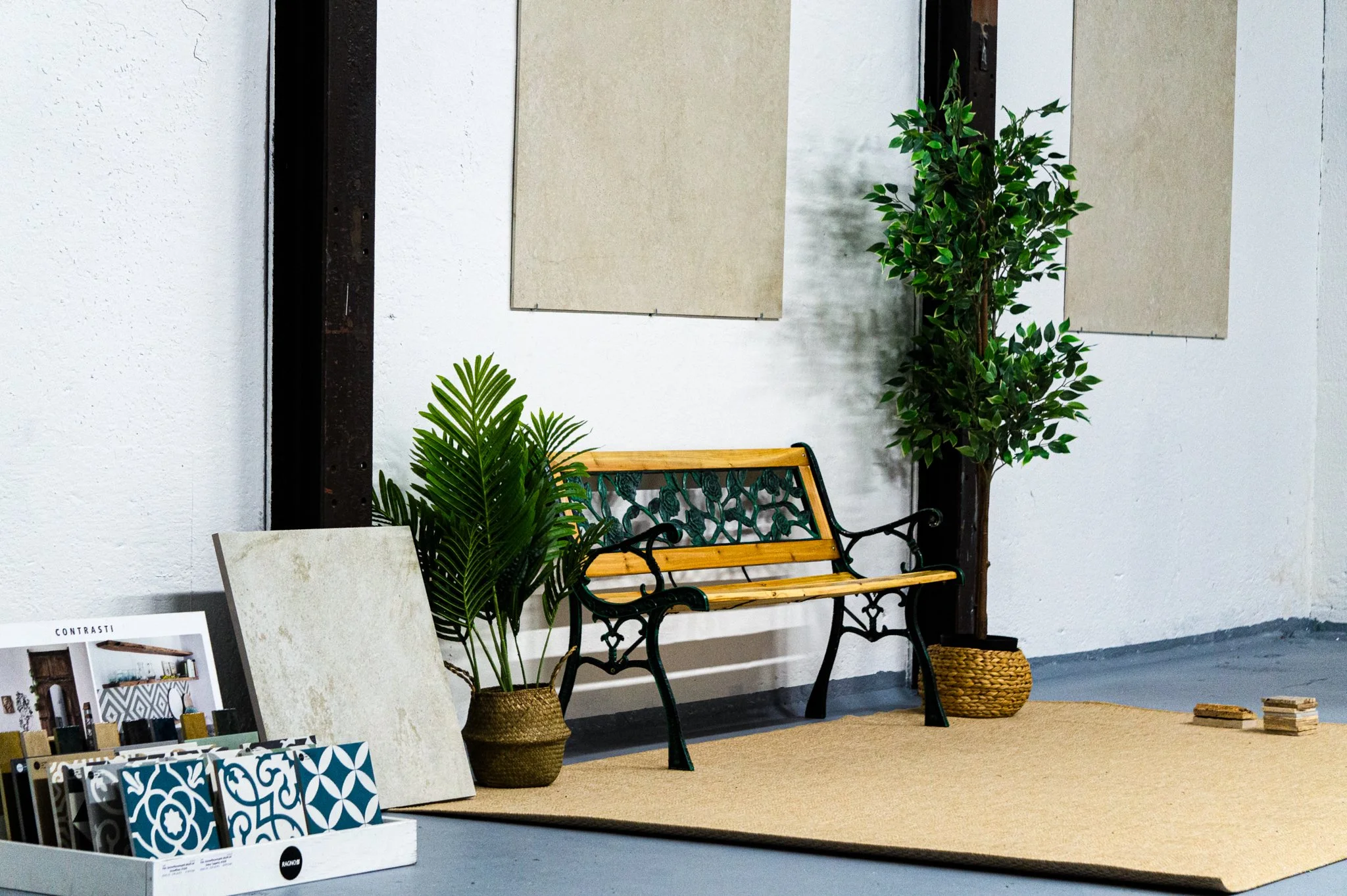 Ein Raum mit Sitzbank, zwei große Pflanzen in Körben, Wanddeko und Musterbücher. Aufgenommen von Hilal Studios.
