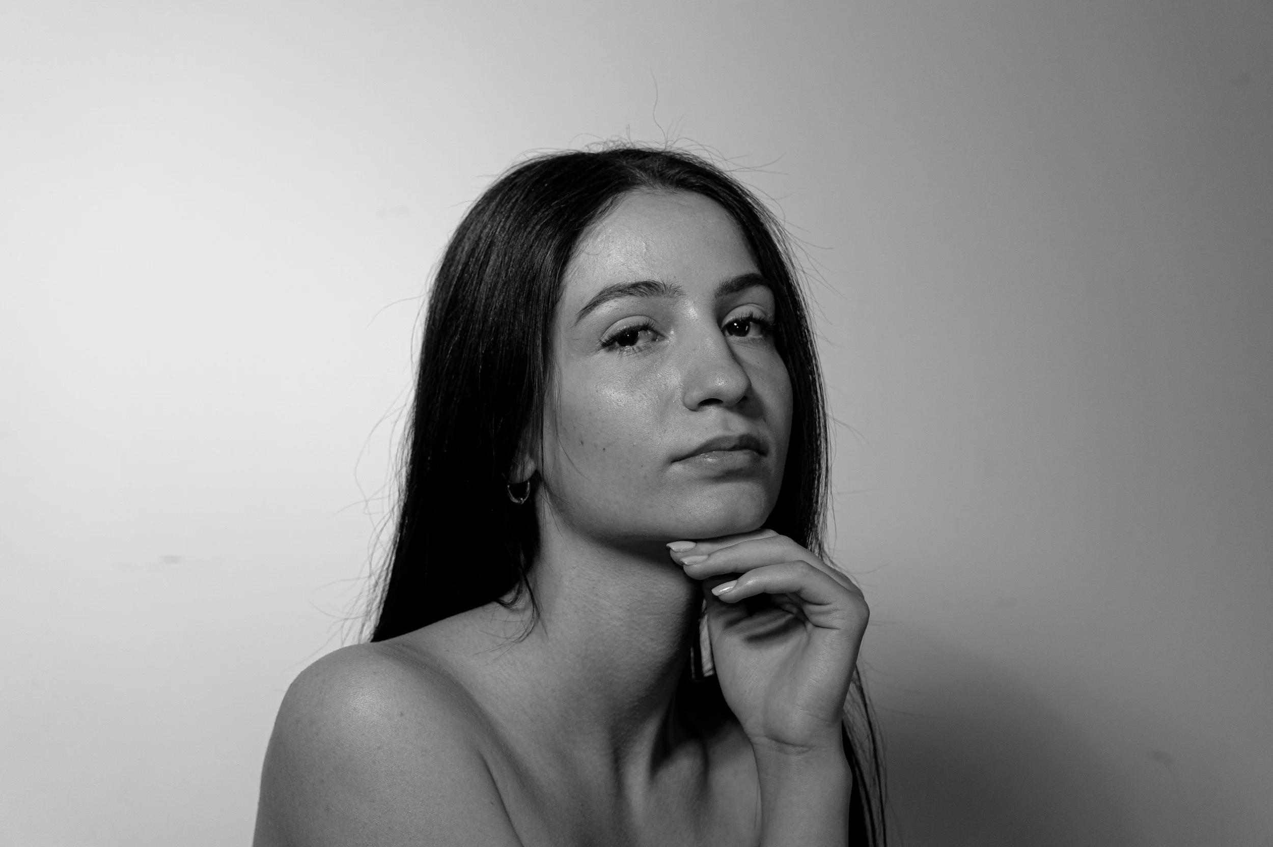 Schwarz-Weiß-Fotografie eines jungen Mädchens mit dunklem Haar, das nachdenklich den Kopf auf die Hand gestützt hat. Aufgenommen von Hilal Studios.