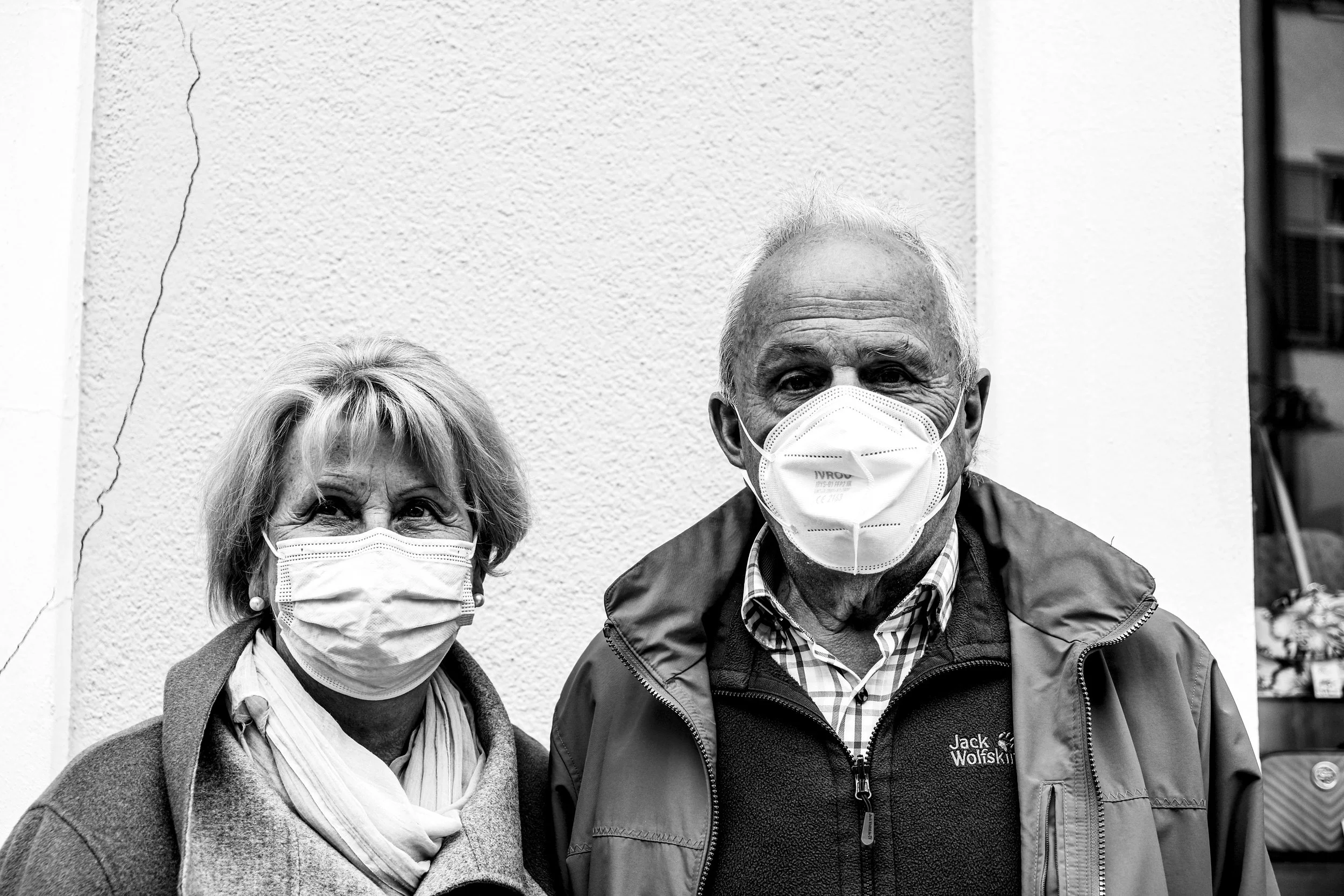 Ein älteres Paar trägt Gesichtsmasken und steht vor einer weißen Wand. Aufgenommen von Hilal Studios.