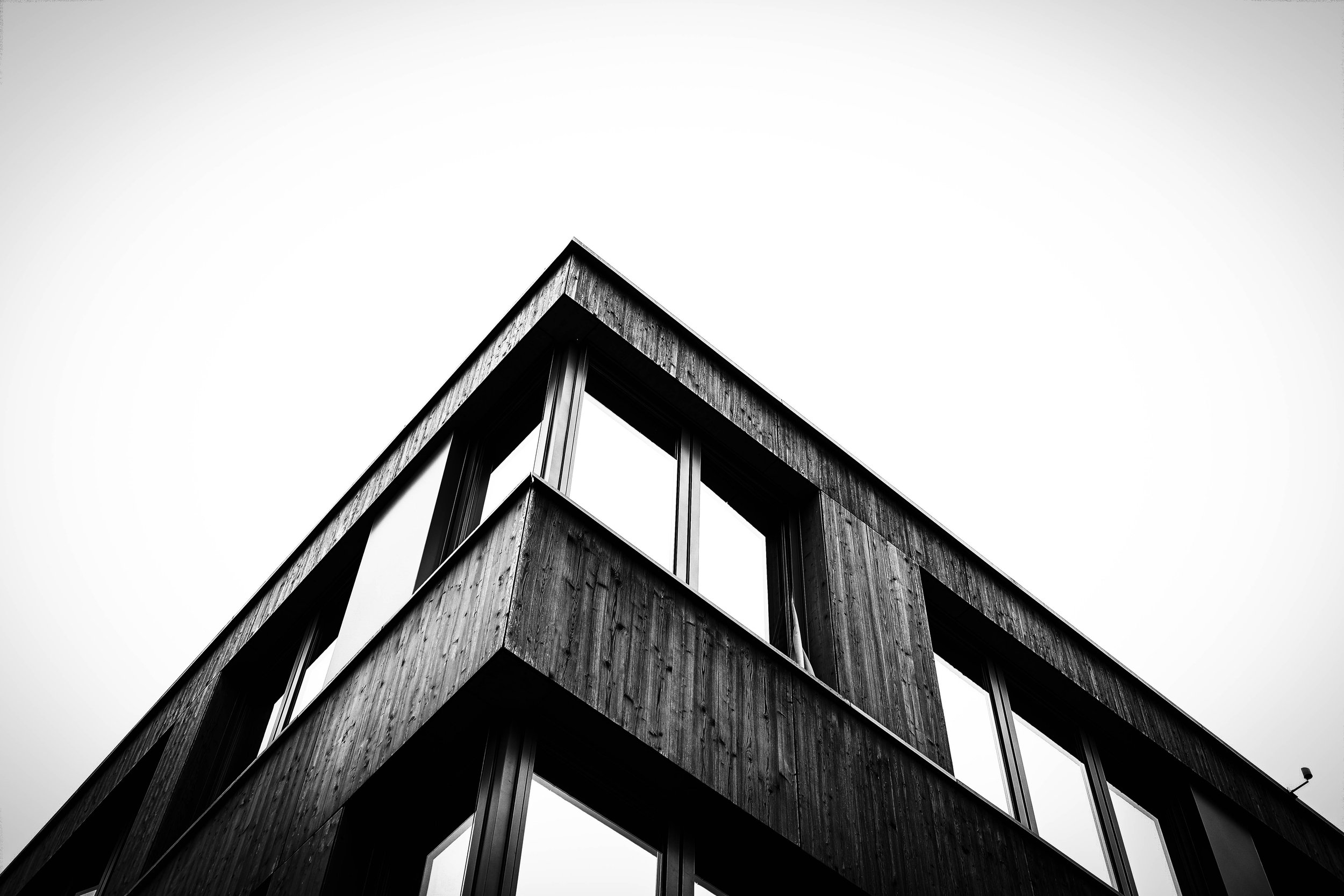 Schwarz-weiß-Foto eines modernen Gebäudes mit Holzfassade und großen Fenstern, aufgenommen aus ungewöhnlichem Blickwinkel. Aufgenommen von Hilal Studios.