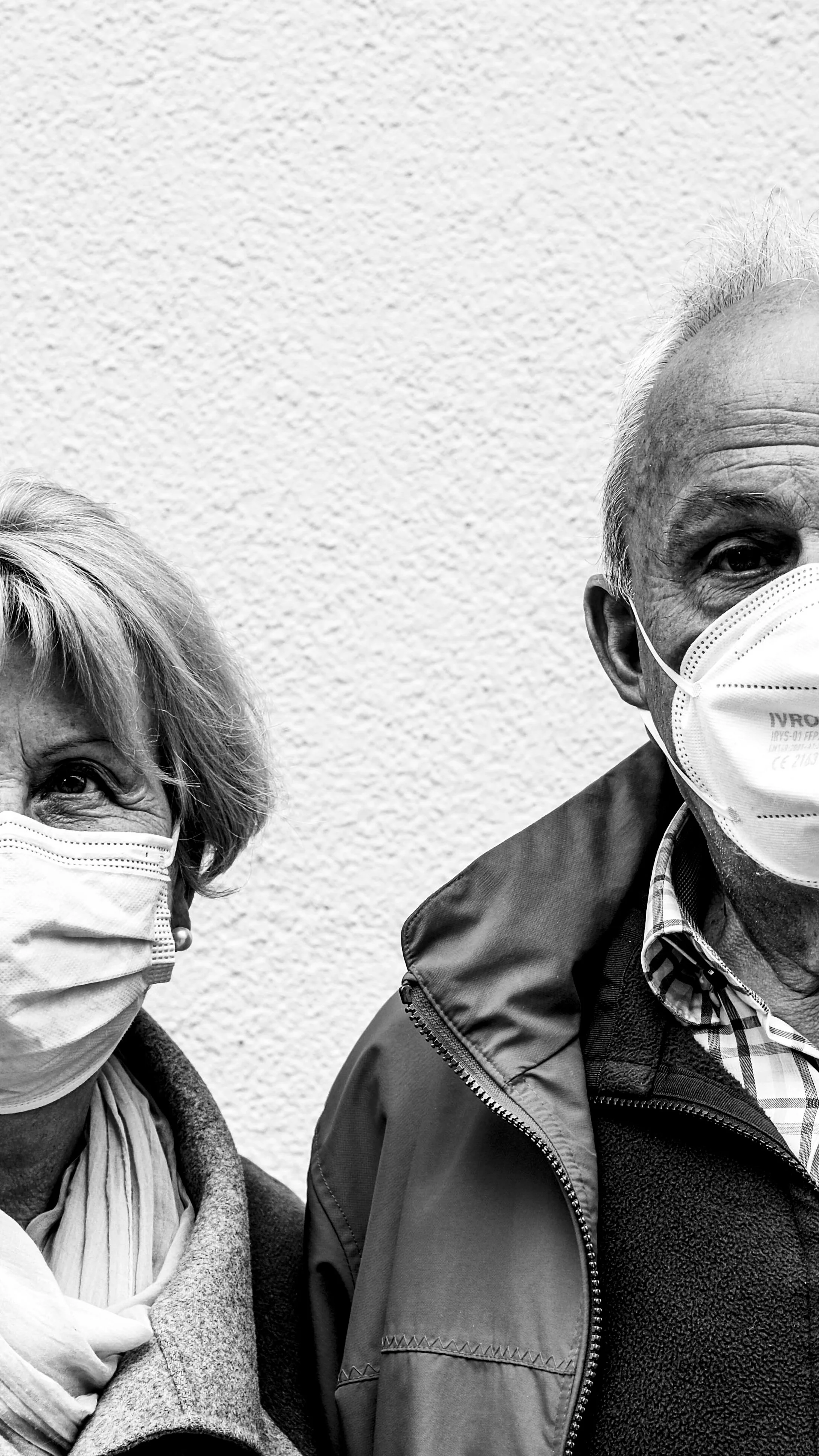 Das Bild zeigt eine älteren Mann und eine ältere Frau, beide tragen Gesichtsmasken und stehen vor einer weißen Wand. Aufgenommen von Hilal Studios.