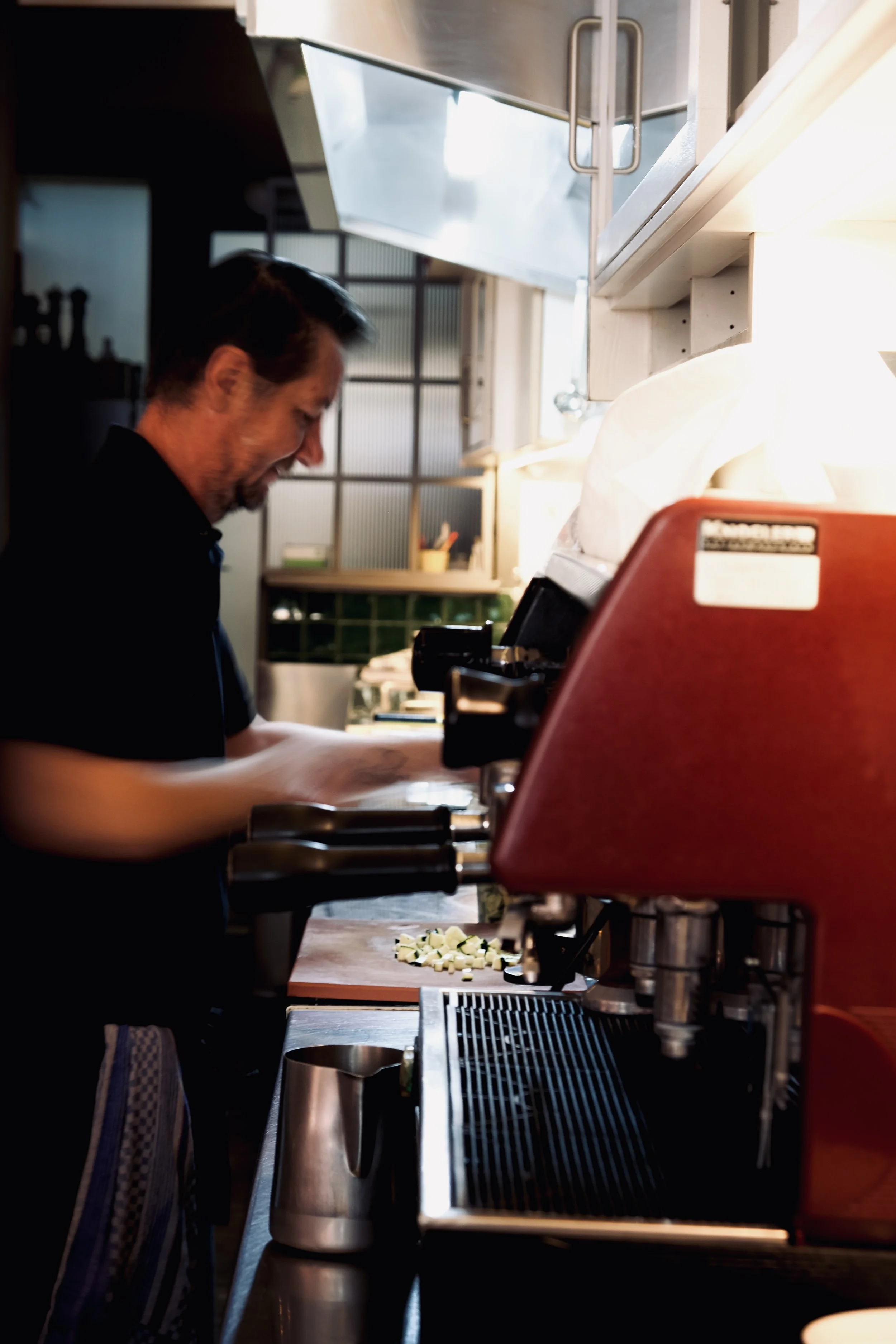 Ein Mann arbeitet in einer Restaurantküche hinter einer Espressomaschine, während er Kaffeebohnen mahlt. Aufgenommen von Hilal Studios.