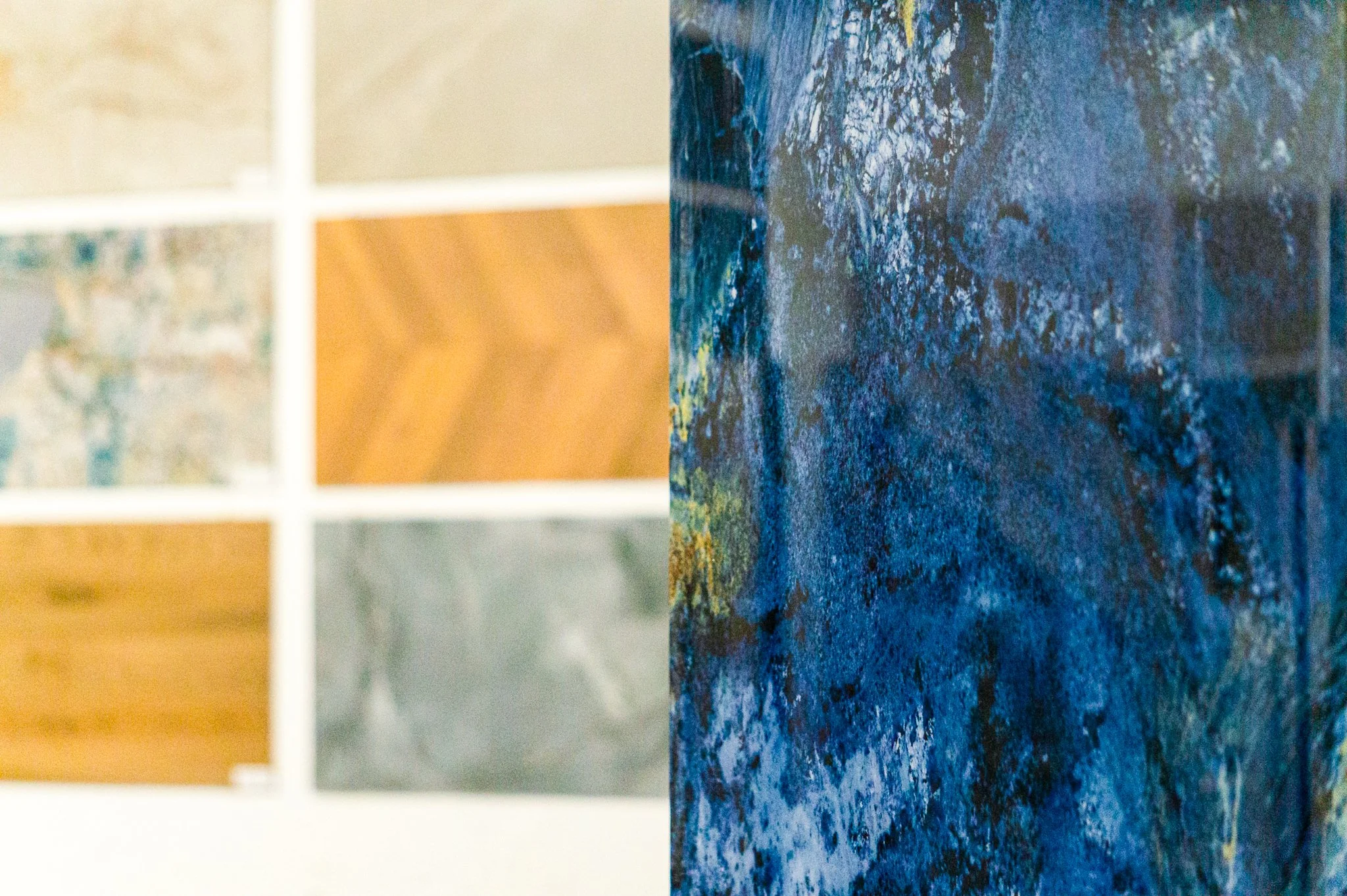 Mehrere Fliesen mit unterschiedlichen Mustern und Farben, darunter Holzoptik, Marmor, und ein abstraktes blaues Gemälde. Aufgenommen von Hilal Studios.