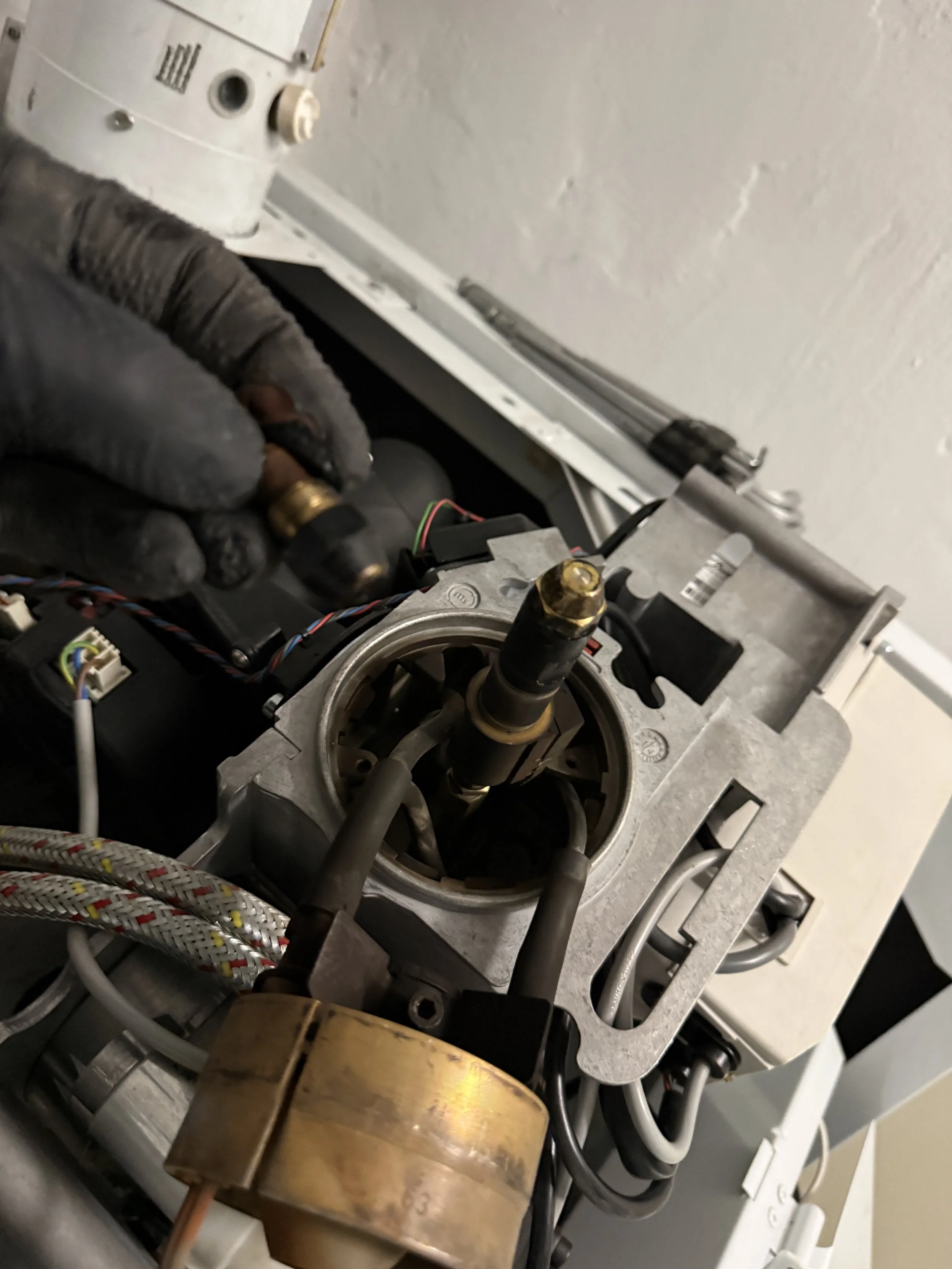 Ein Handwerker in schwarzen Handschuhen arbeitet an einem mechanischen Gerät, das anscheinend Teil einer Maschine ist, mit diversen Kabeln und Komponenten.