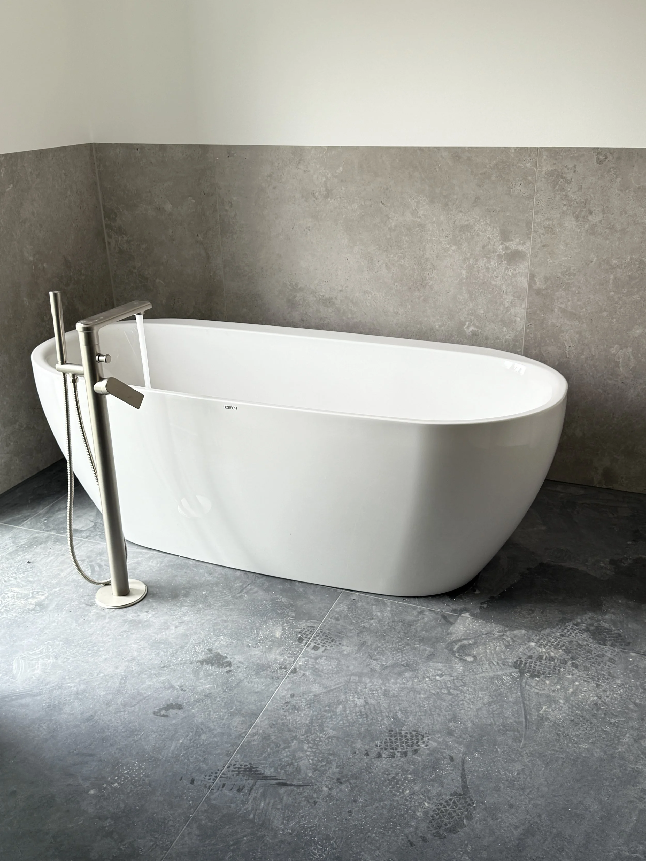 Moderne, freistehende Badewanne in einem Badezimmer mit grauen Fliesen auf Fußboden und Wandstücken