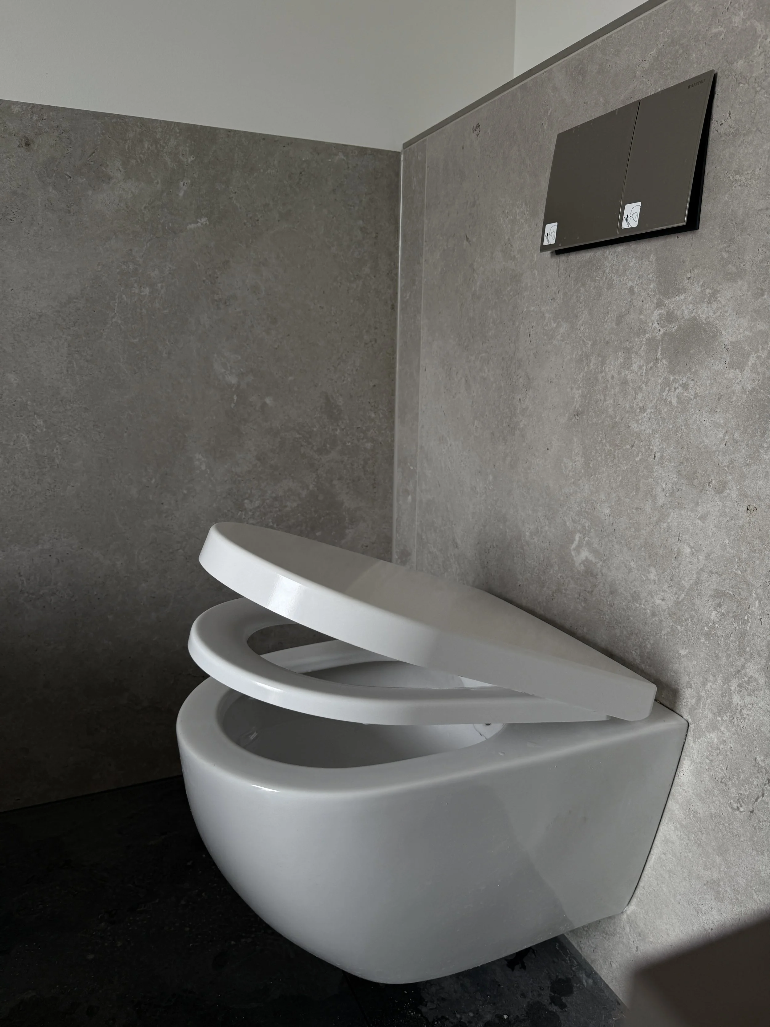 Moderne weiße Toilette mit offenem Sitz in einem Badezimmer mit grauen Wänden.