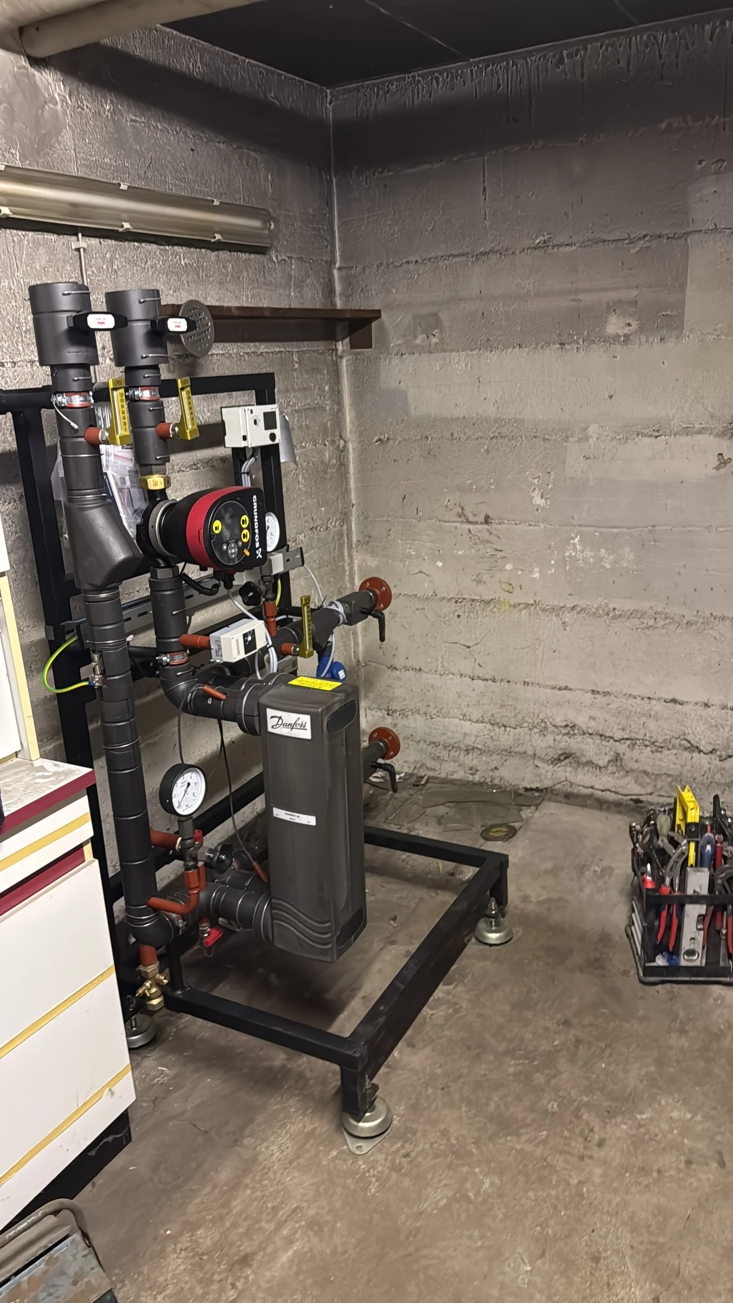 Installation eines Heiz- oder Wassersystems mit Pumpe, Rohren, Druckmessern und Werkzeugen in einem Kellerraum.
