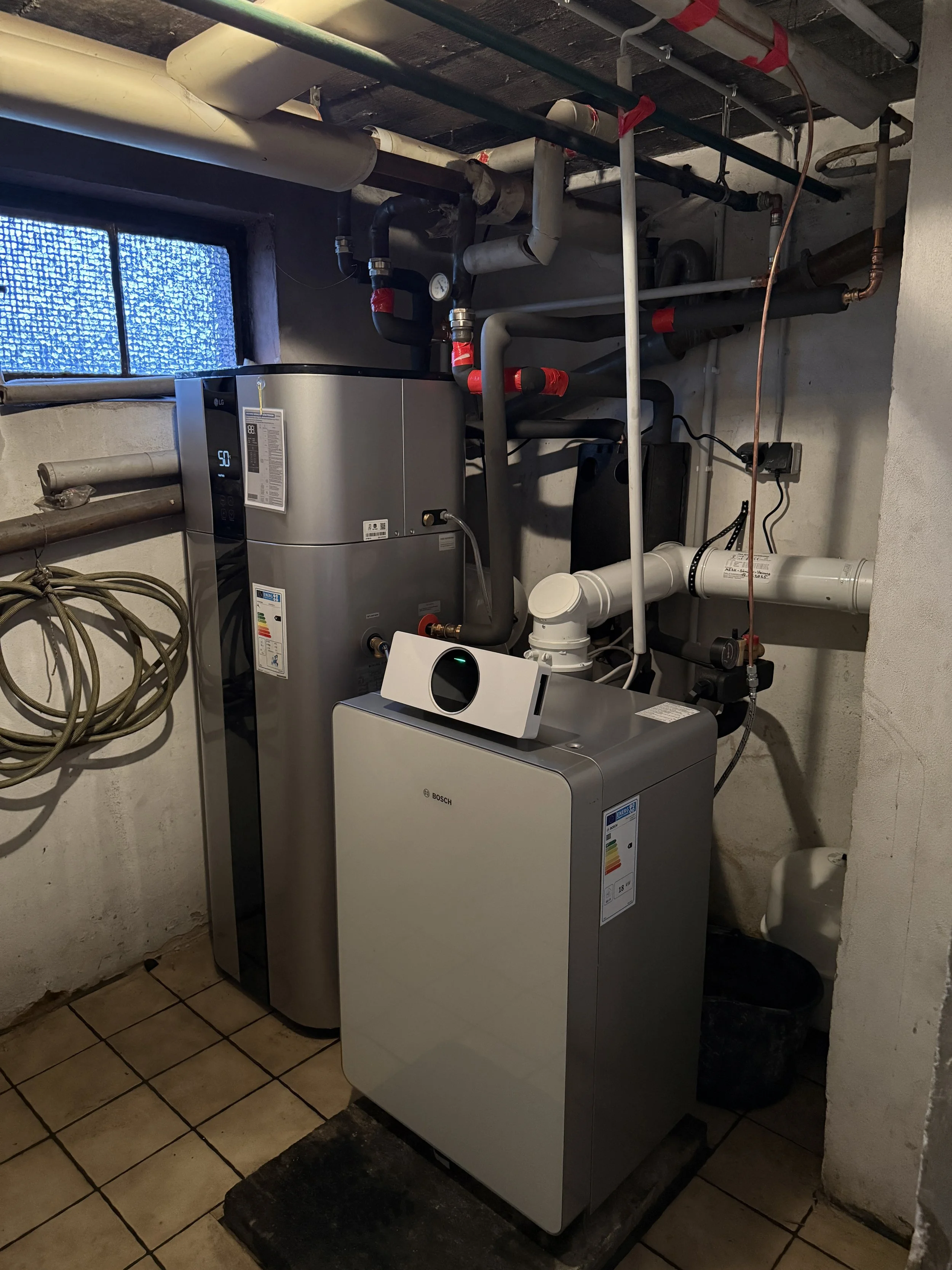 Ein Hauskeller mit Heizungs- und Wasserversorgungssystem, einschließlich eines Warmwasserbereiters, eines Waschmaschinen und verschiedener Rohrleitungen.