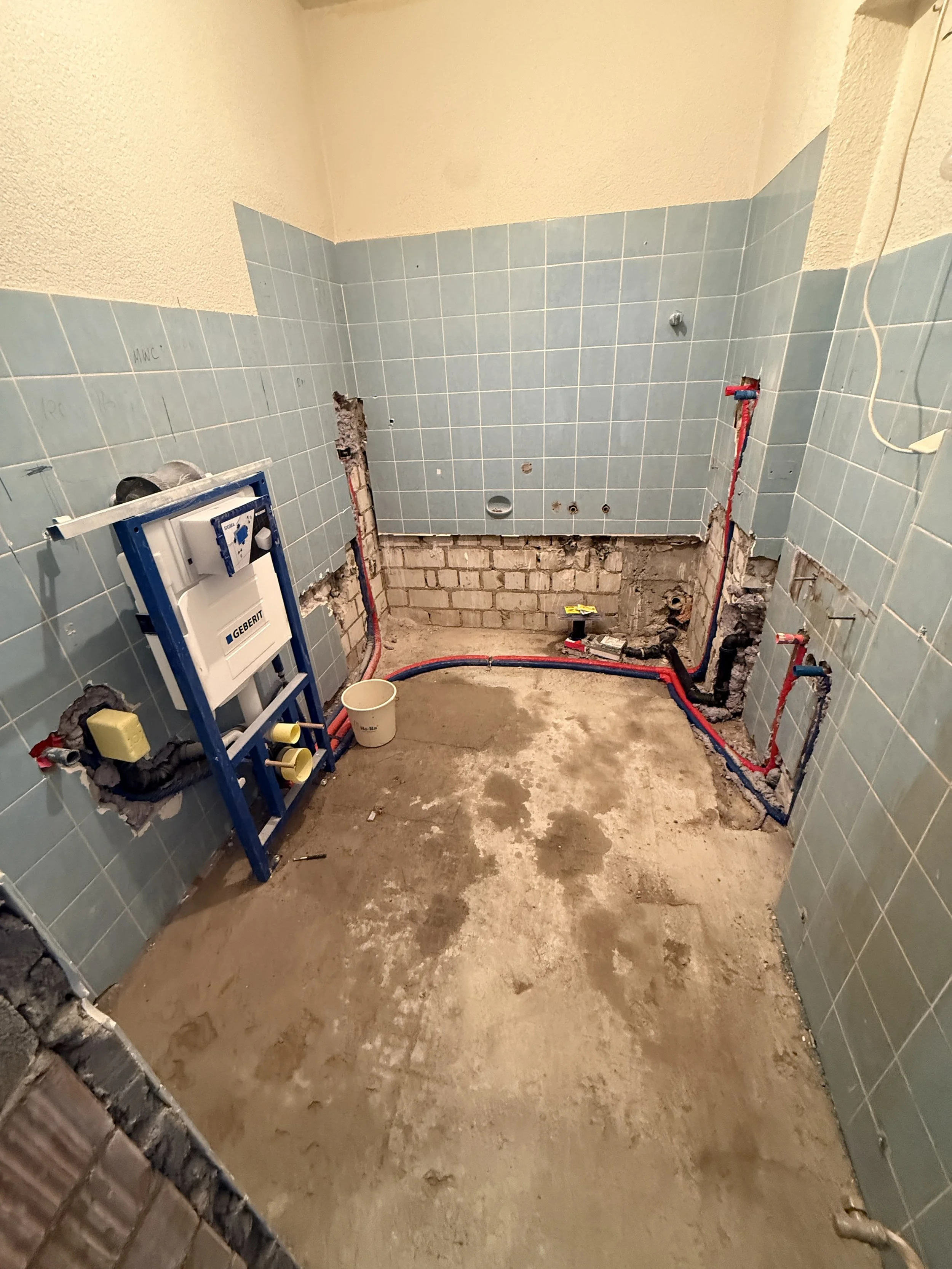 Ein Badezimmer im Umbau mit blauen Wandfliesen, geöffneten Rohrleitungen und Rohren, die für Sanitärinstallationen vorbereitet werden.