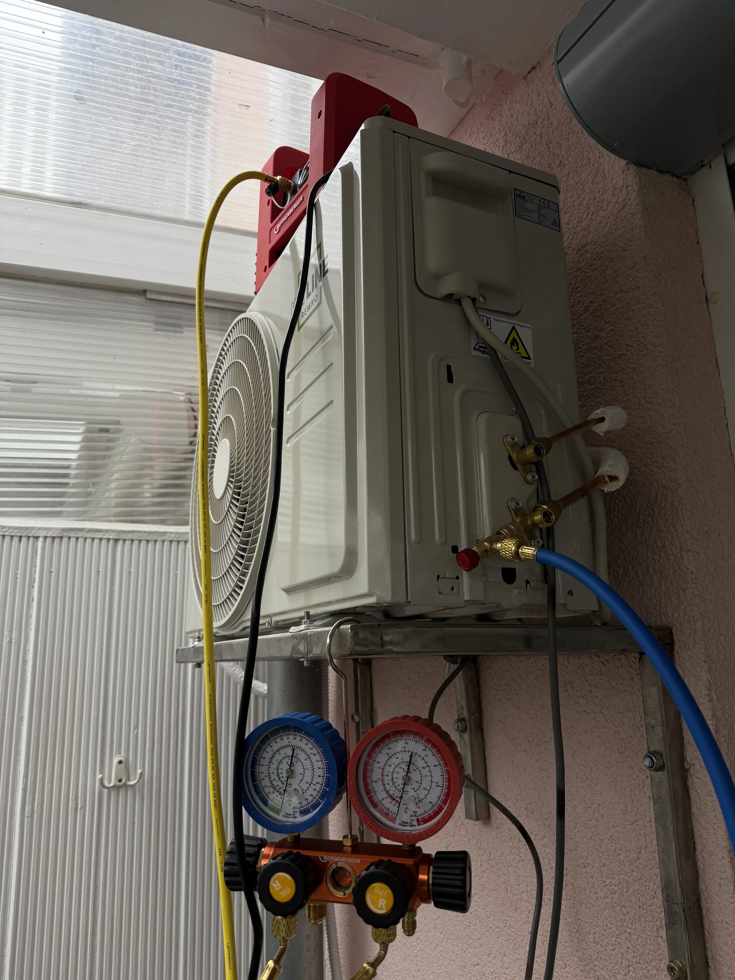 Klimaanlage mit Messgeräten, Schläuchen und Steuerung an einer Wand.