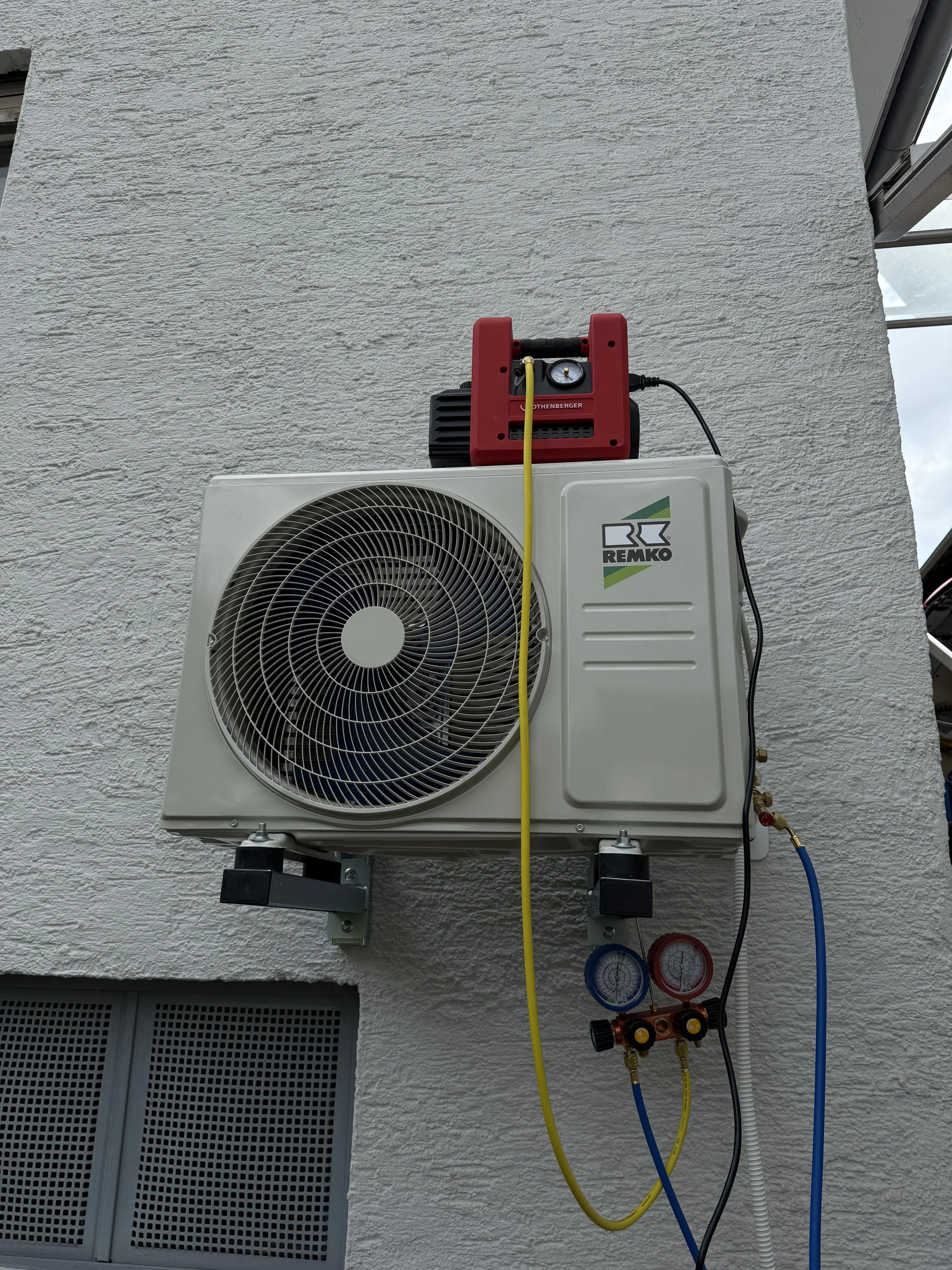 Klimaanlagen-Außengerät an einer Hauswand mit Mess- und Wartungsausrüstung, einschließlich Manometer und Druckschläuchen.