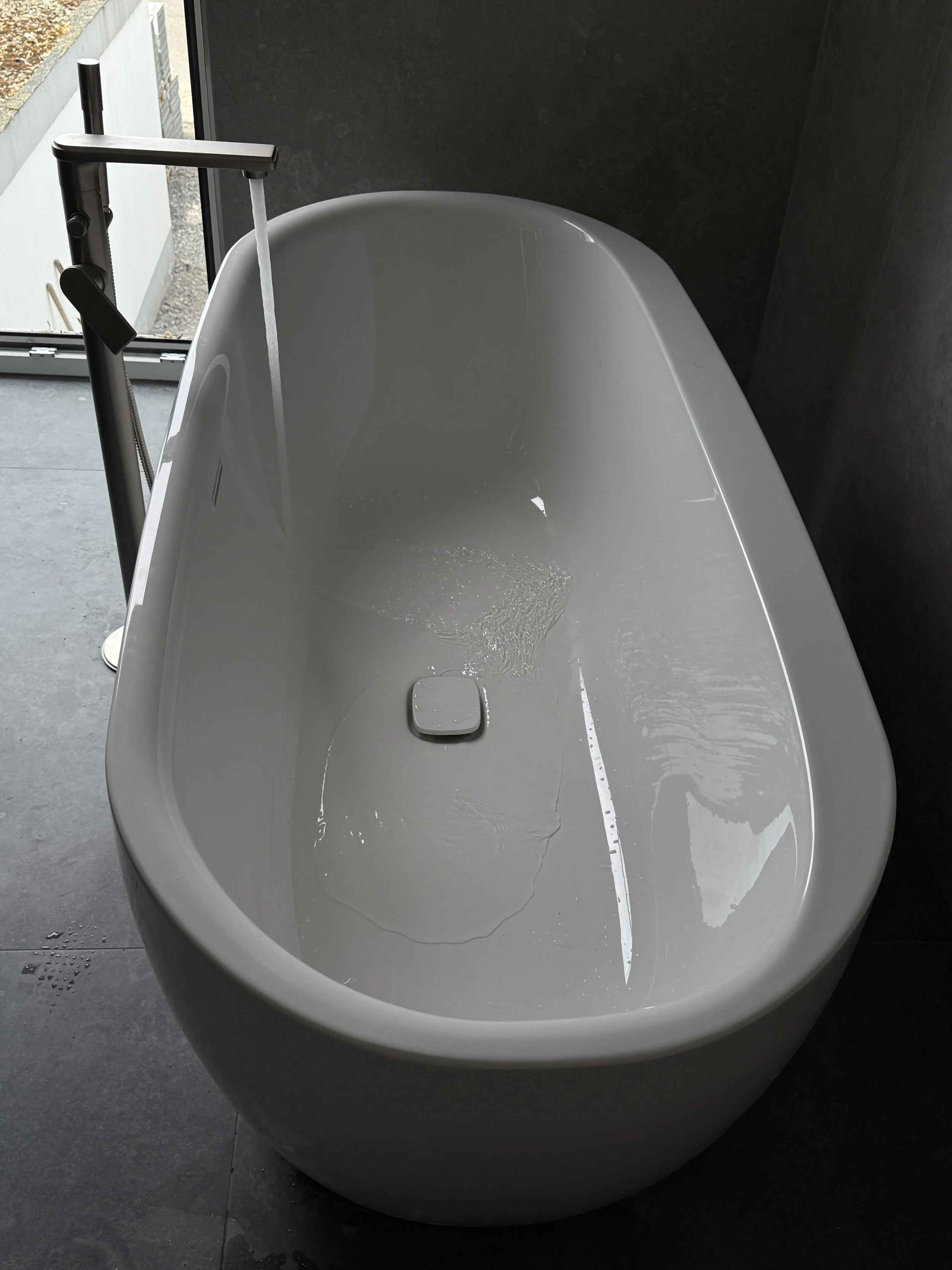 Weiße Badewanne in einem Badezimmer mit dunklen Wänden und Fliesen, Wasser läuft aus dem Wasserhahn