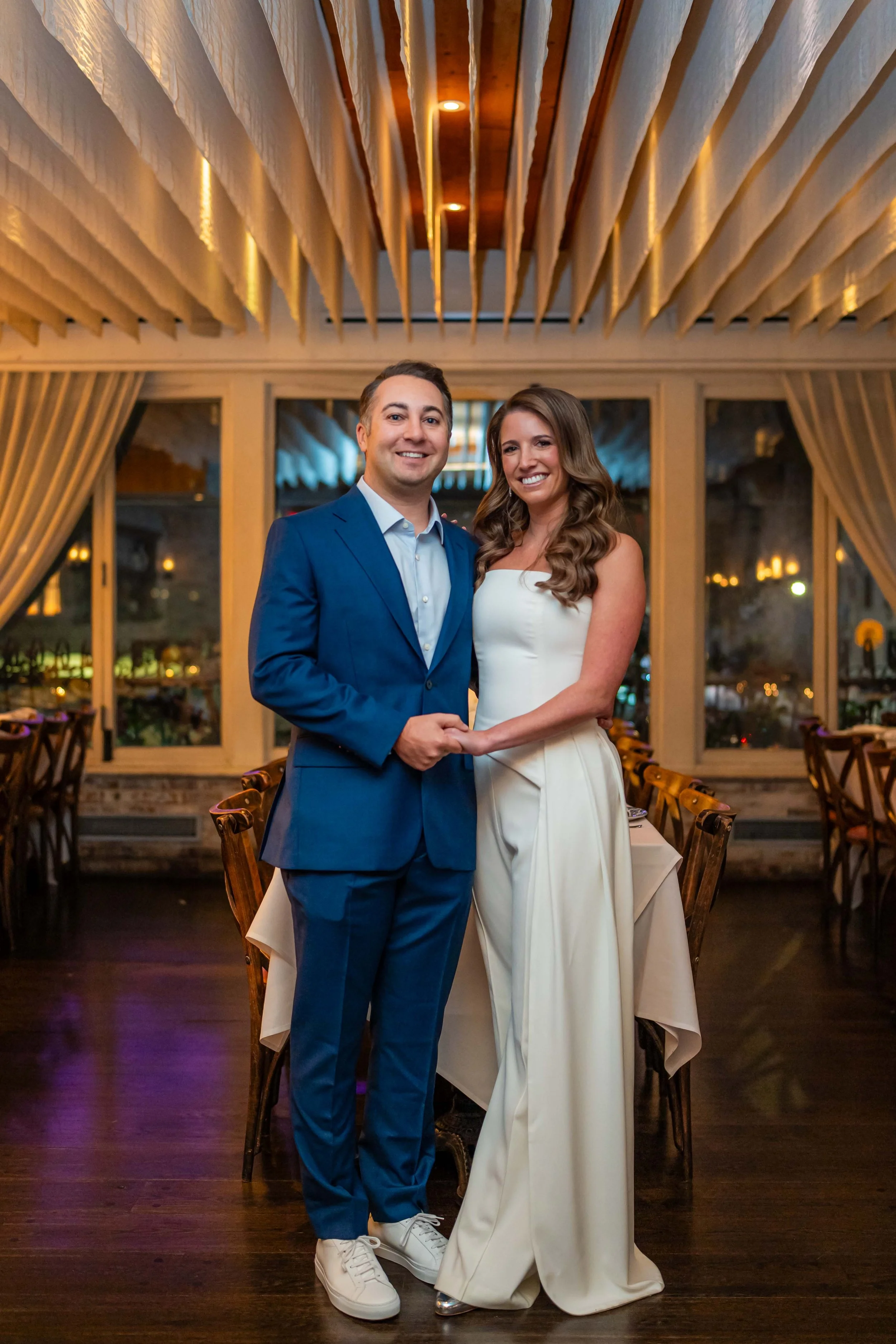 A couple dressed formally posing in a stylish, modern restaurant interior, with elegant ceiling decor and ambient lighting.