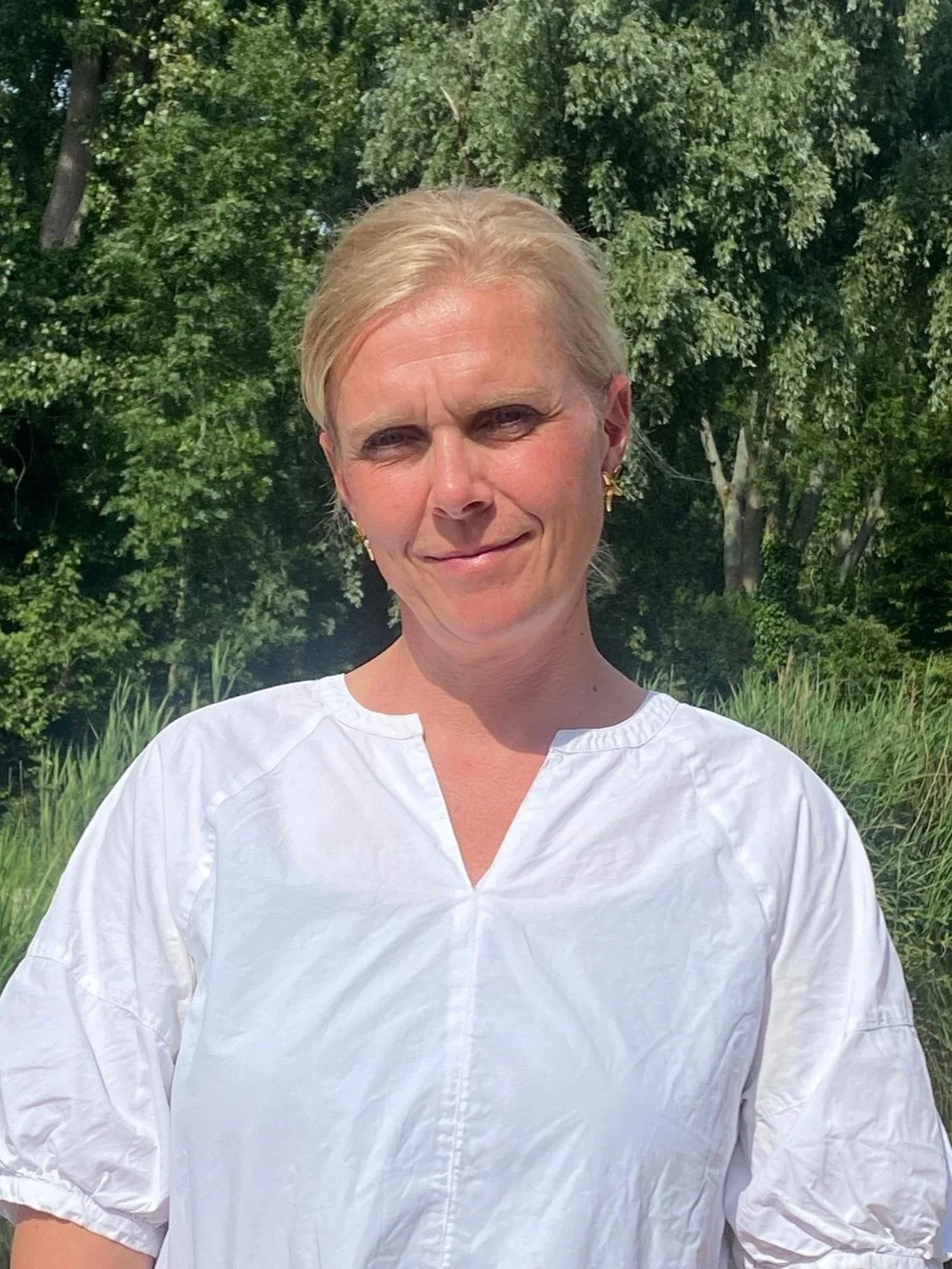 Inge staand buiten met groene bomen in de achtergrond.