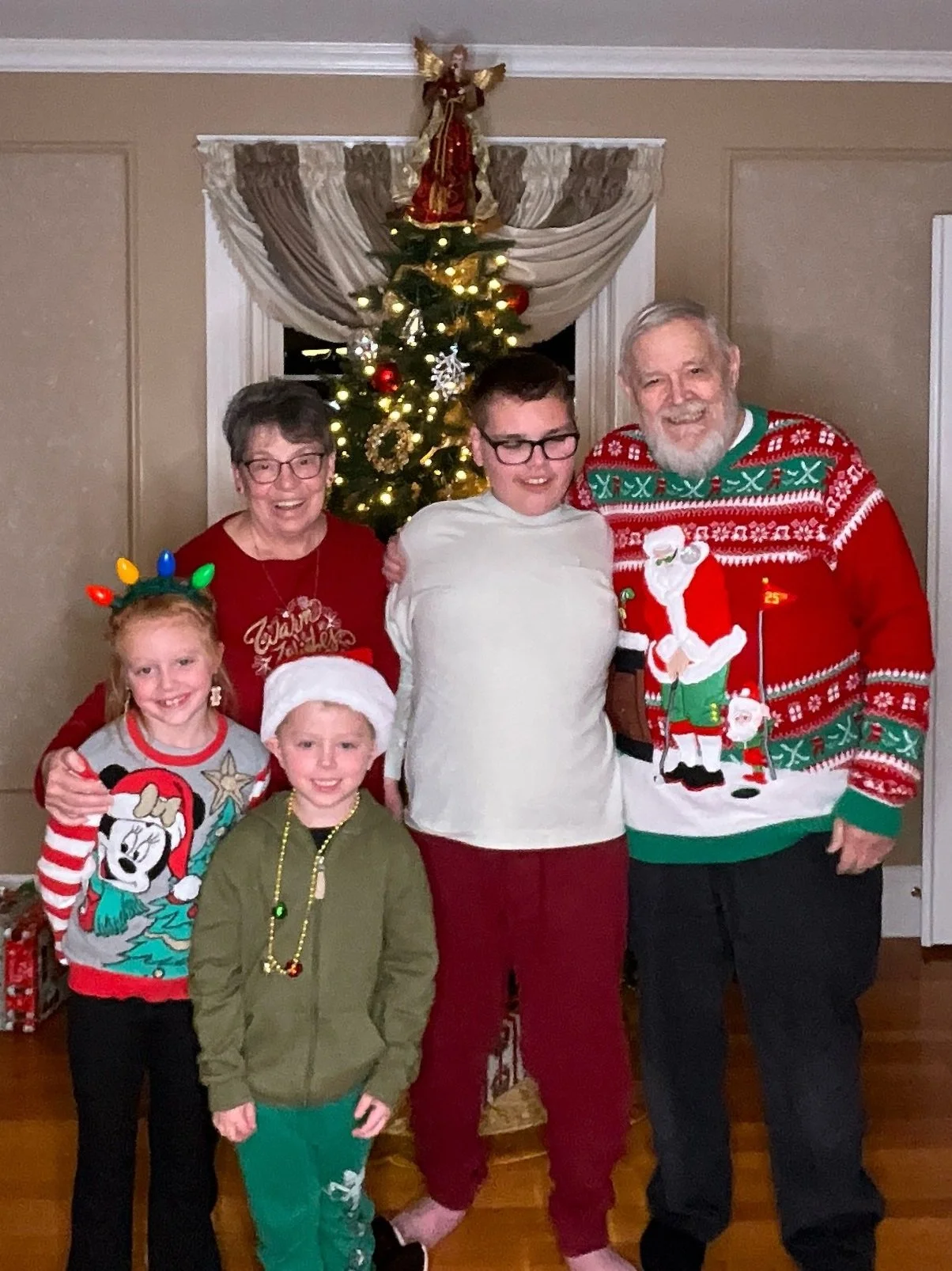 Family gathered in front of a decorated Christmas tree, wearing holiday sweaters and accessories, celebrating Christmas.