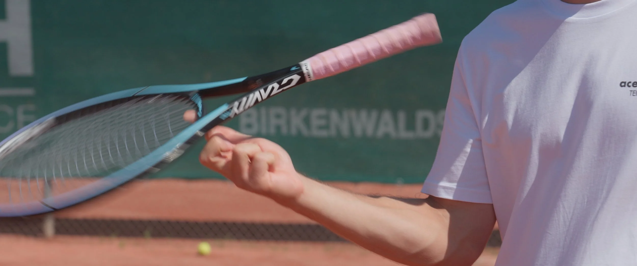 Close-up of a tennis player's hand holding a tennis racket with a tennis ball on the clay court.